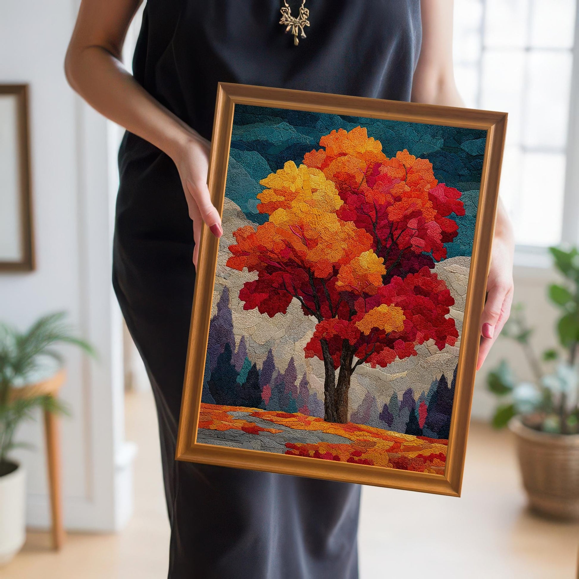 A person in a black dress holds up a framed print of an autumn tree. The frame is a deep, warm orange. The artwork shows a tree with a blend of red and gold leaves.