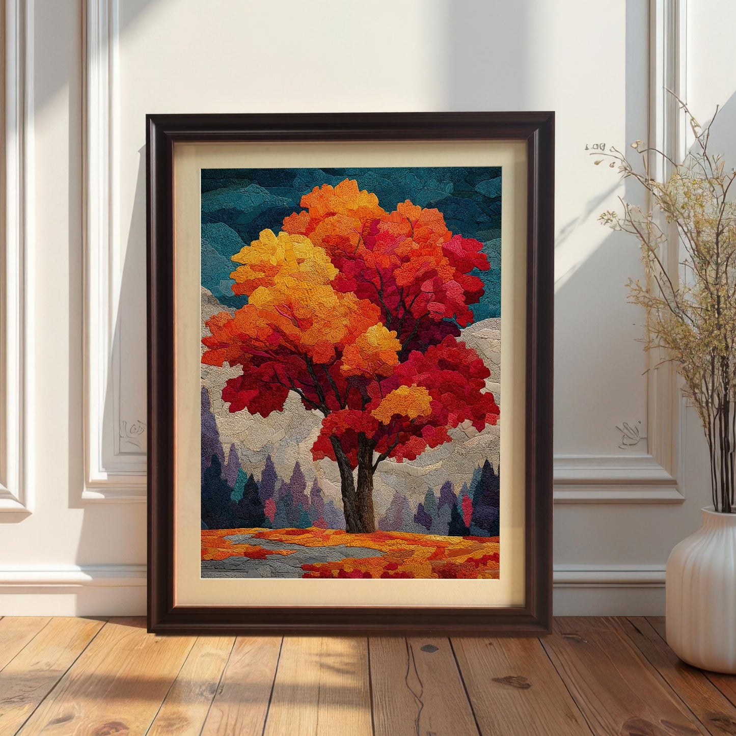 A framed, abstract painting of an autumn tree with a black frame and white mount sits on a wooden floor, leaning against a white wall. Next to it is a white vase with dried flowers.