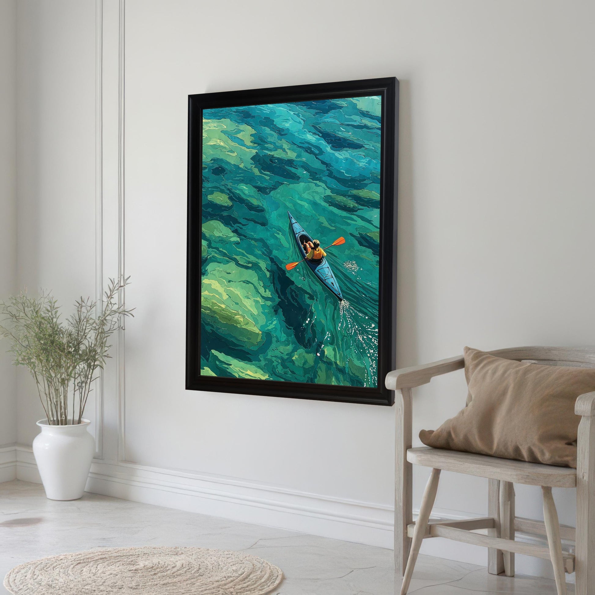 A black-framed art print of a person in a kayak on clear, turquoise water hangs on a white wall in a bright room.