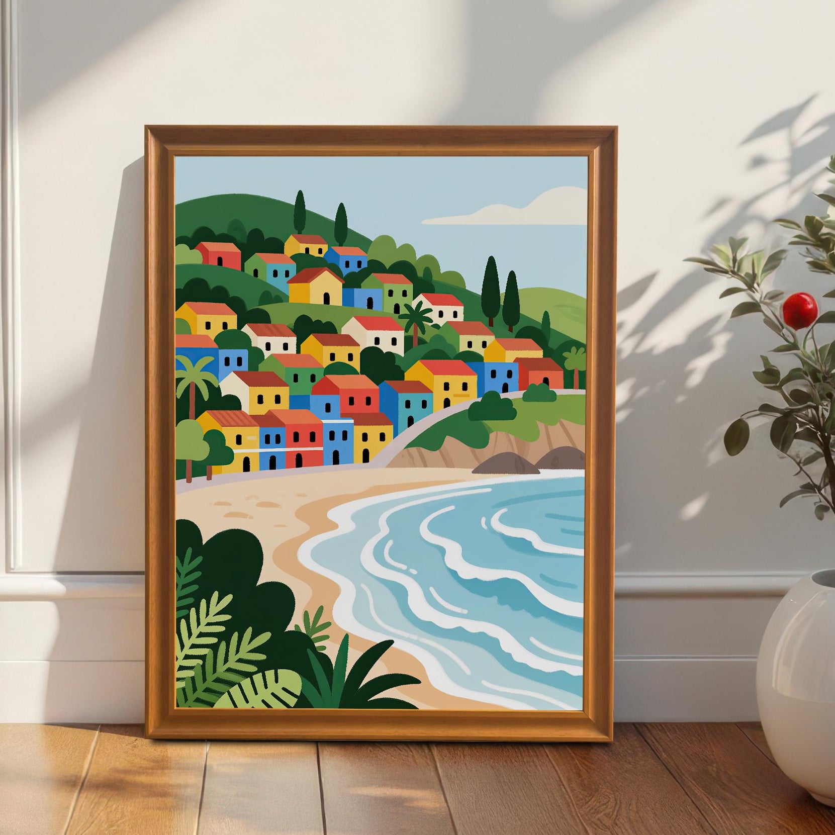 A framed painting of a village with colorful houses on a hill overlooking a beach. The painting is in an orange frame and leans against a white wall next to a potted plant with red berries.
