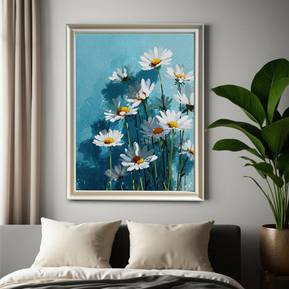 A framed art print of white daisies on a blue background, with a white frame, hanging on a gray wall above a bed with a plant next to it.