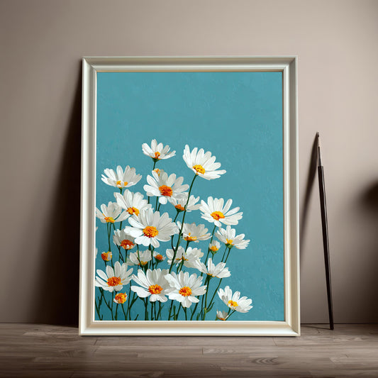 A white-framed art print of white daisies with yellow centers on a teal background leans on a wood floor next to a single paintbrush.