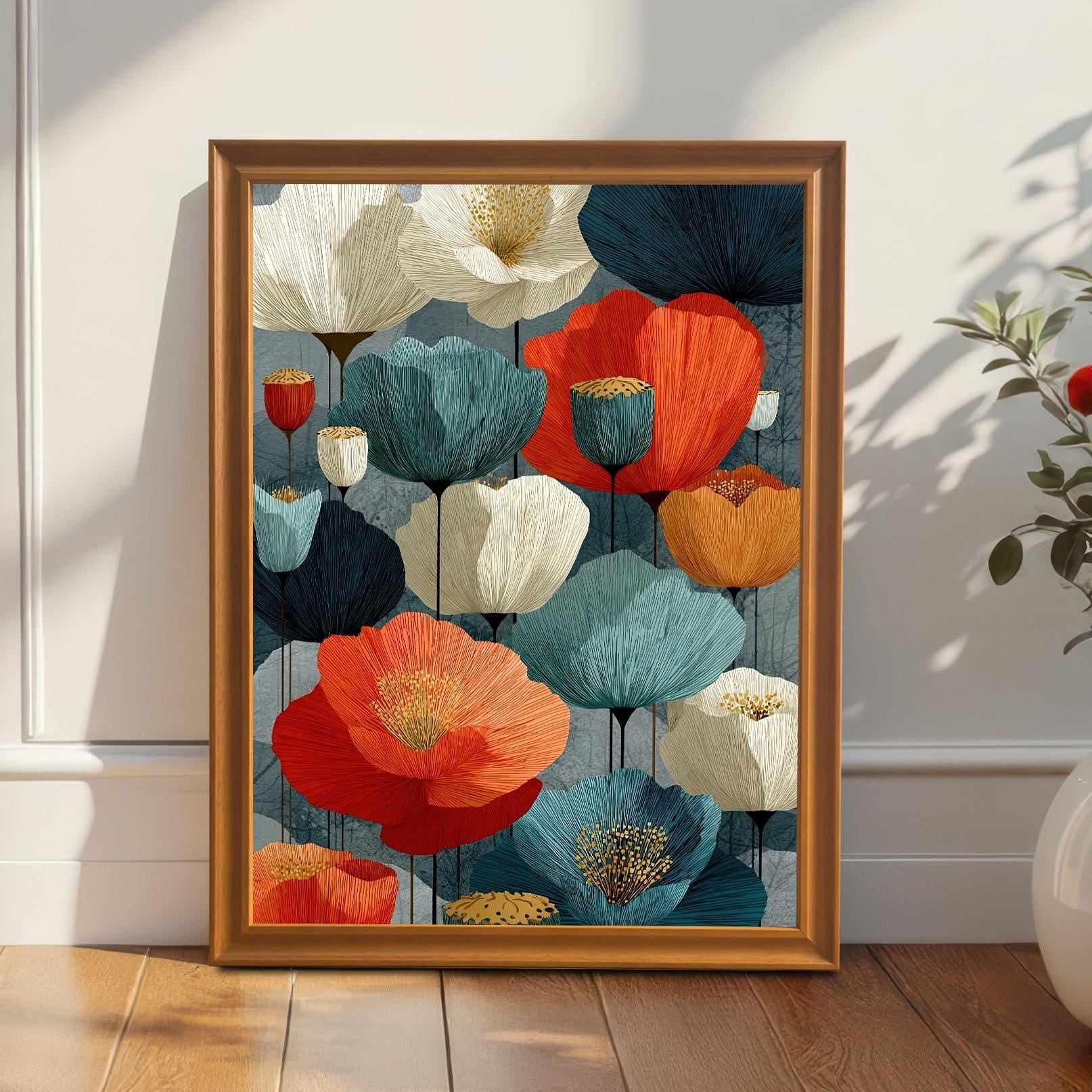 A framed art print with an abstract design of flowers in shades of red, white, orange, and blue. The print is leaning against a white wainscoted wall with sunlight casting shadows.