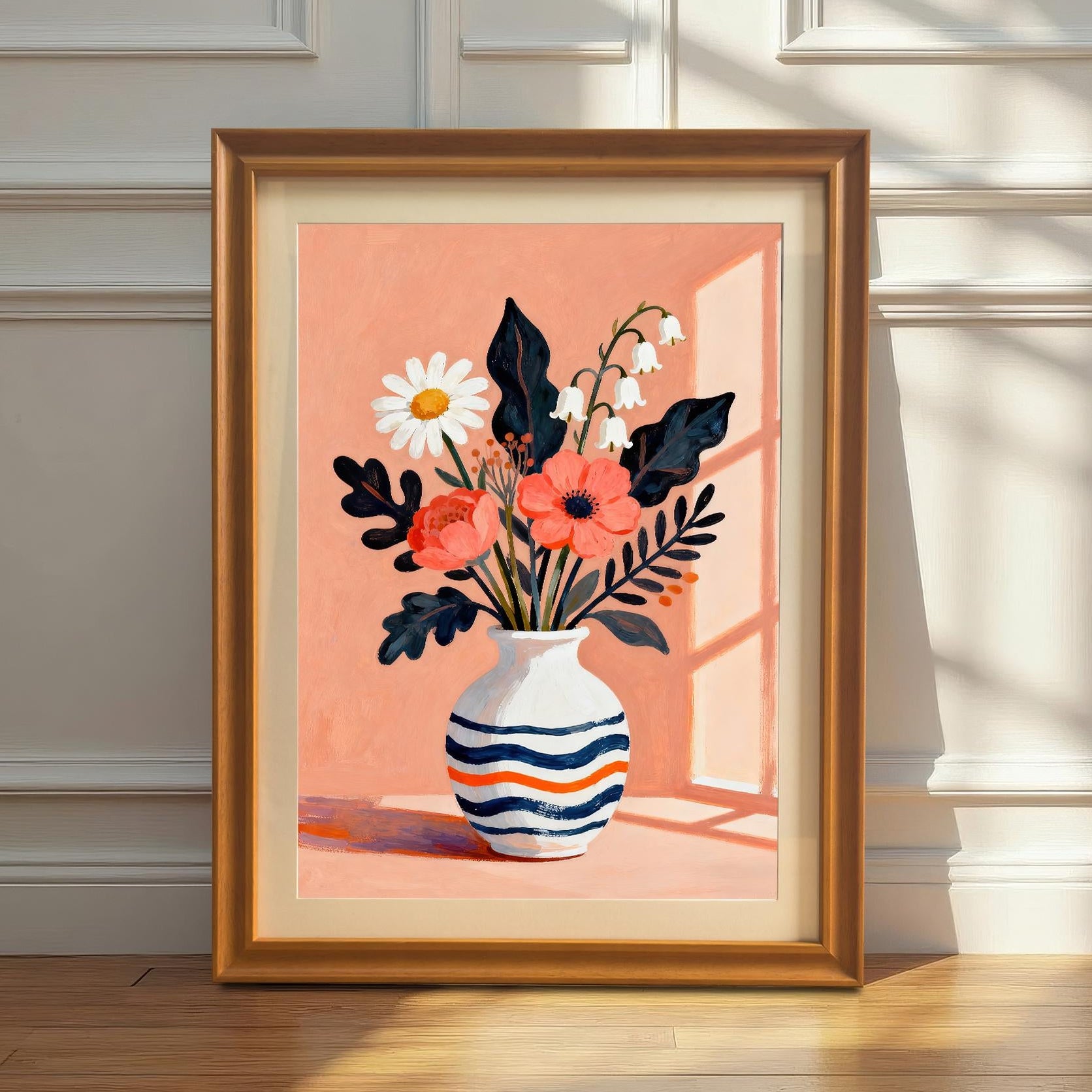 A framed art print featuring a vase of flowers with a light orange background. The print is leaning against a white wainscoted wall on a hardwood floor, with sunlight casting a shadow.
