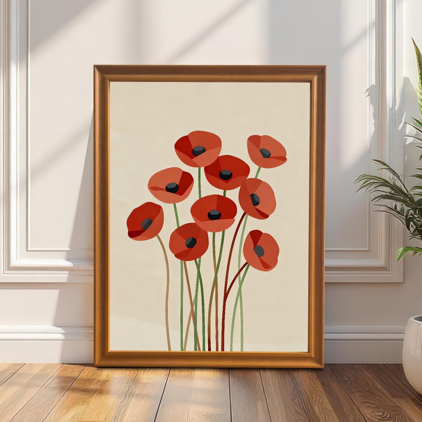 A framed abstract poppy print with a warm wooden frame rests on a floor, leaning against a white paneled wall with a plant nearby.