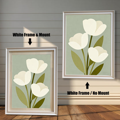 A framed art print of three white tulips is shown in two styles against a wooden wall. One has a white frame with a white mount, the other is a larger size with the same frame, but no mount.