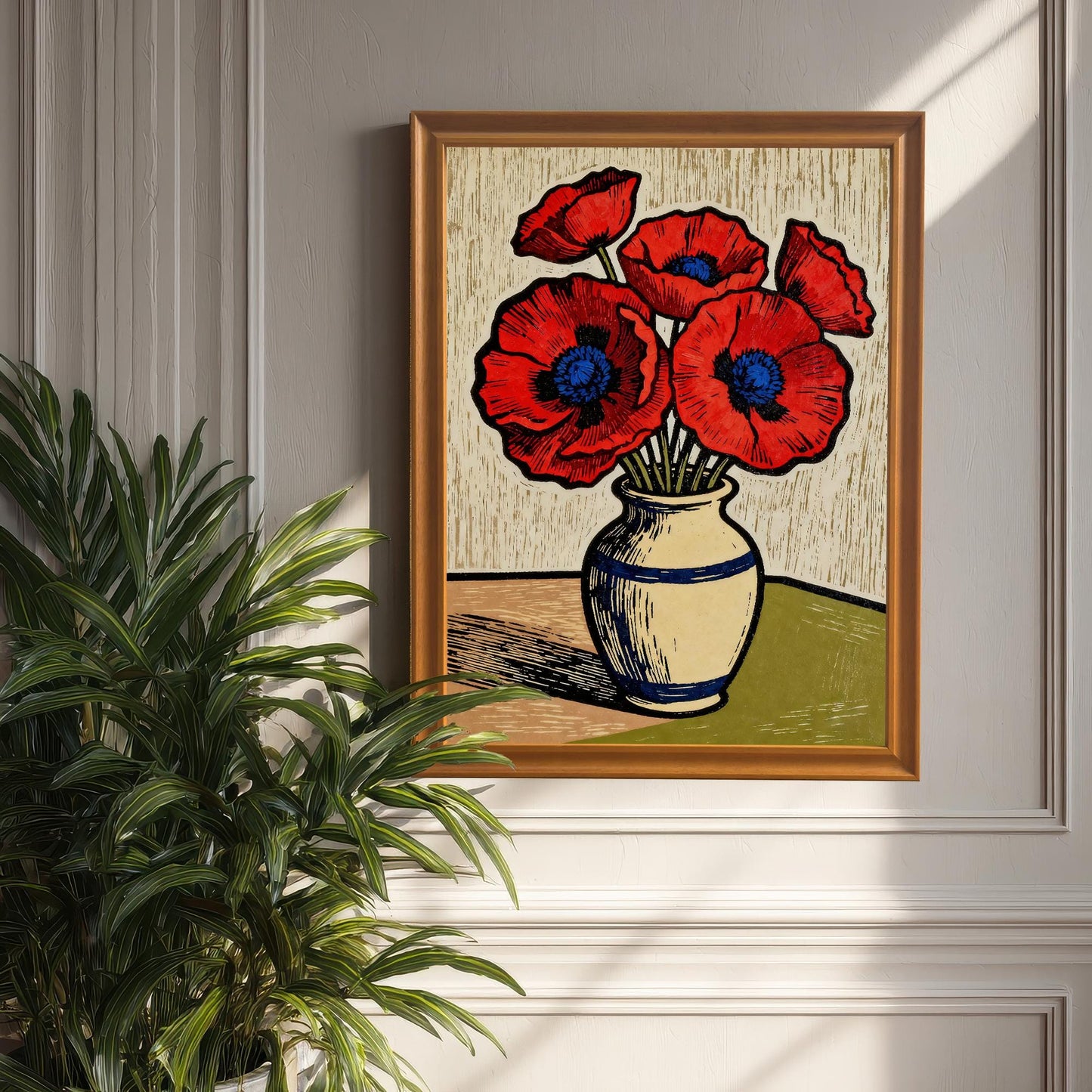 A framed art print of red poppies in an orange frame hangs on a paneled white wall with a large green plant in the foreground. Sunlight casts a bright shadow on the wall.