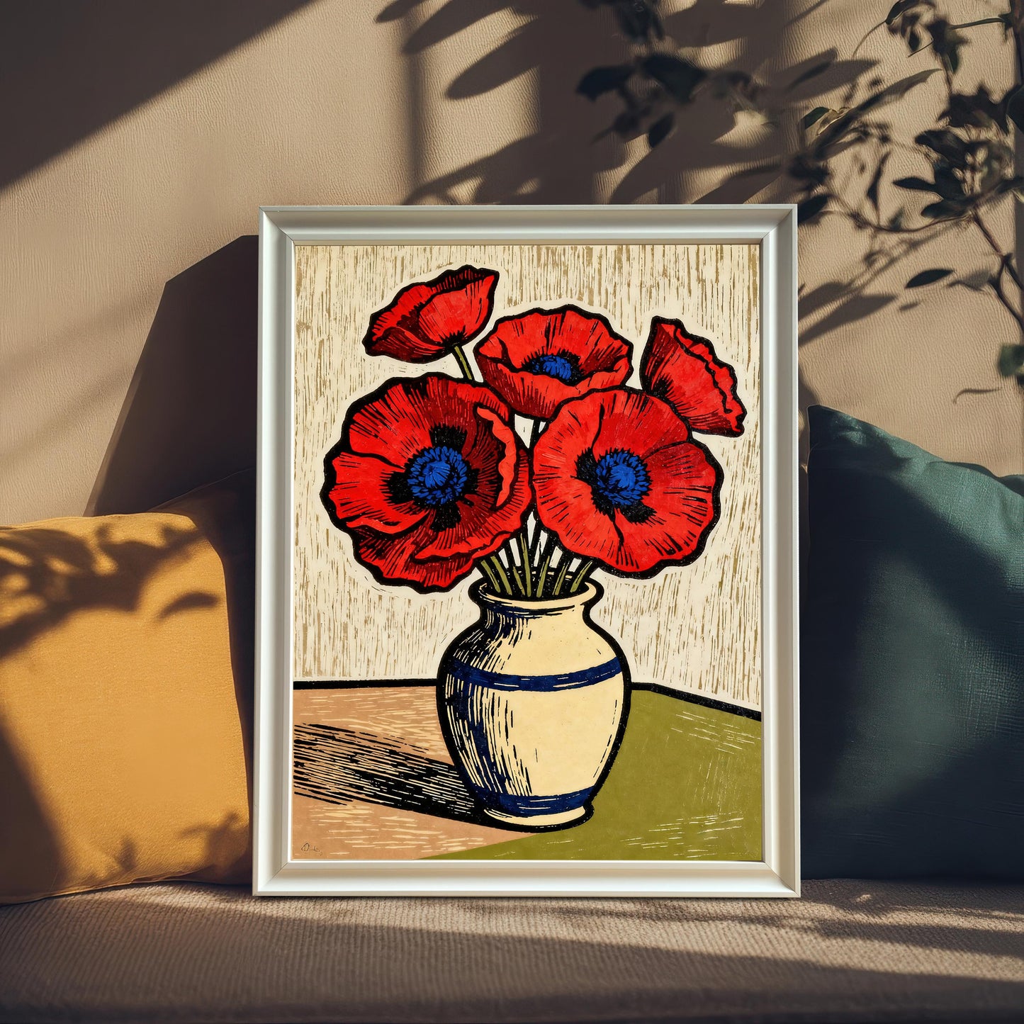 A framed art print of a vase of red poppies. The print is propped on a tan couch between a yellow pillow and a teal pillow, with sunlit shadows of leaves cast over the scene.