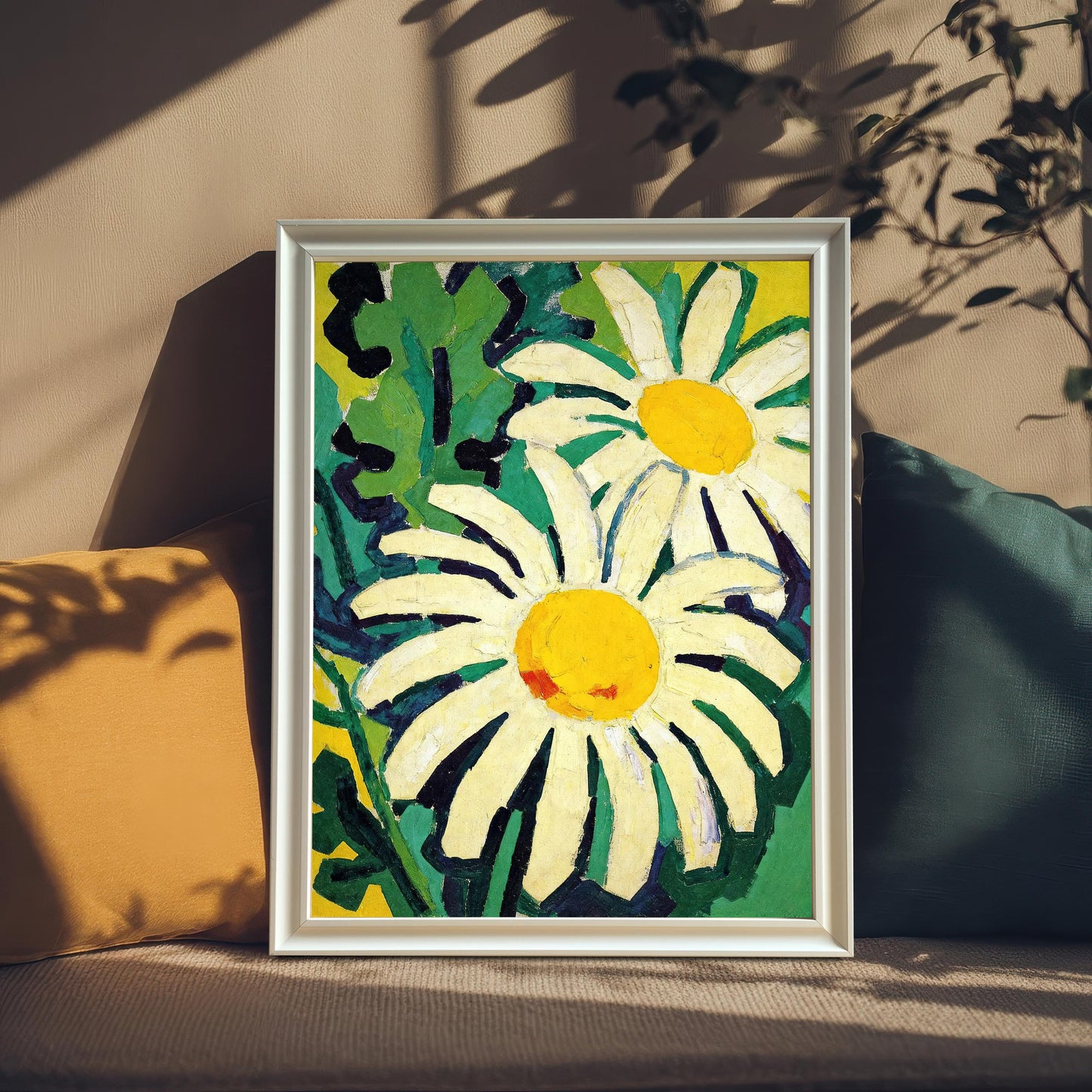 A framed painting of two daisies. The painting is propped on a tan couch between a brown pillow and a teal pillow, with sunlit shadows of leaves cast over the scene.