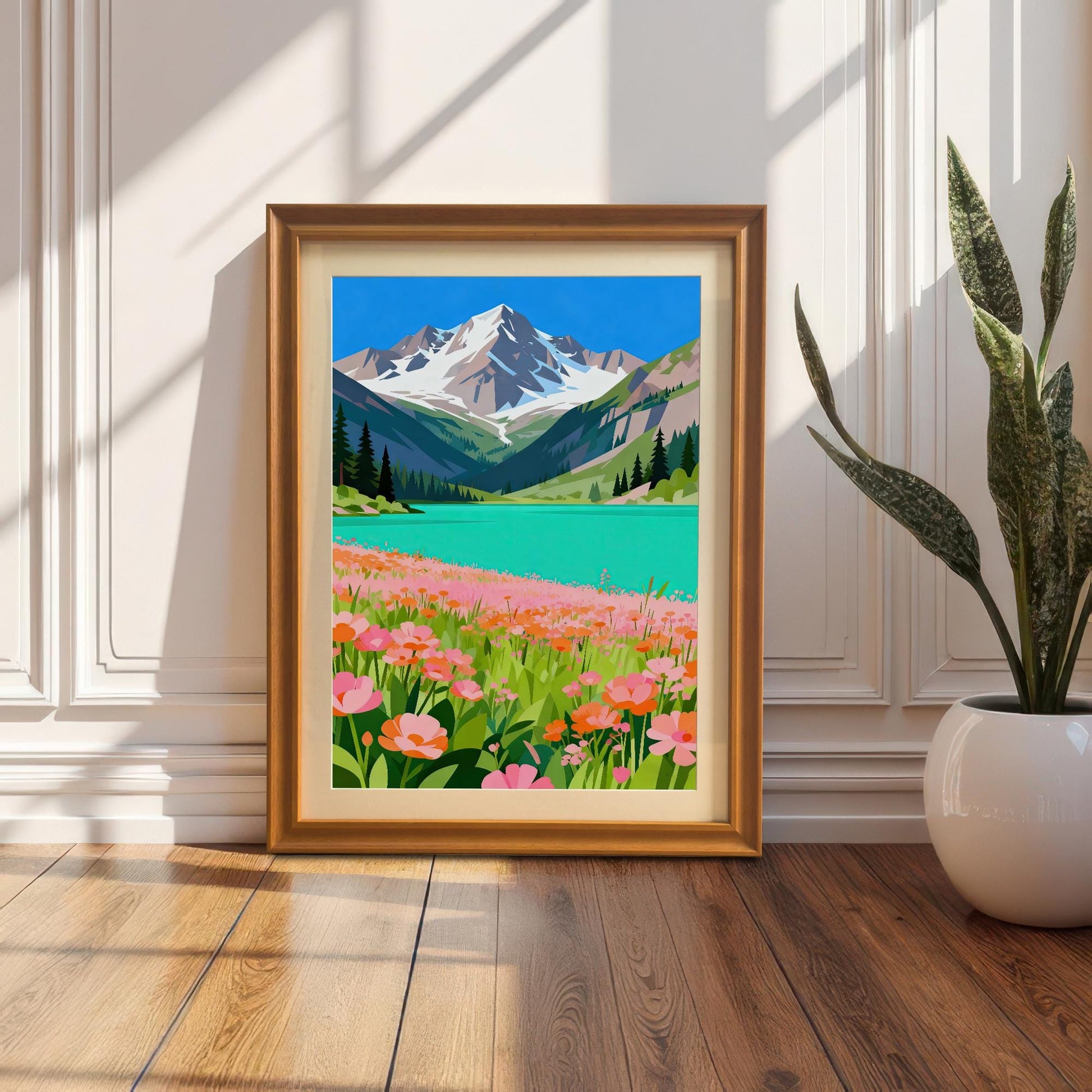 A framed painting of a bright mountain and lake scene. The frame is propped against a white wainscoted wall next to a potted snake plant on a wooden floor.