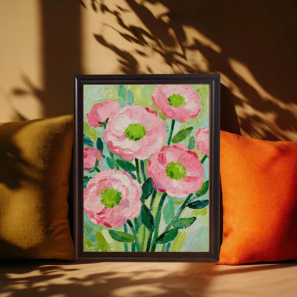 A framed painting of pink flowers in a dark frame propped on a surface between two pillows, with shadows of leaves cast over it.