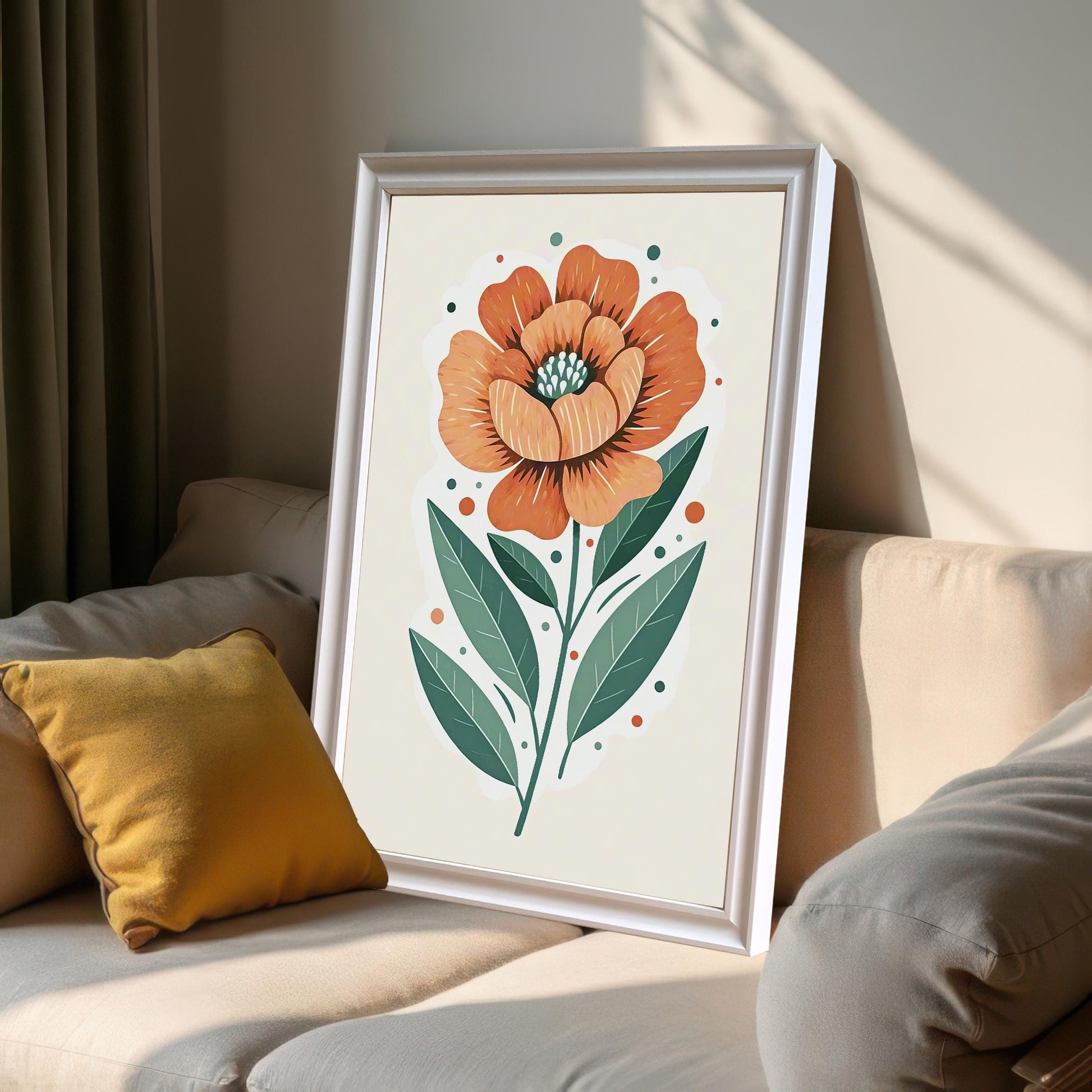 A framed print of a large orange flower with green leaves, leaning against a light-colored couch with a yellow pillow in a sunlit room.