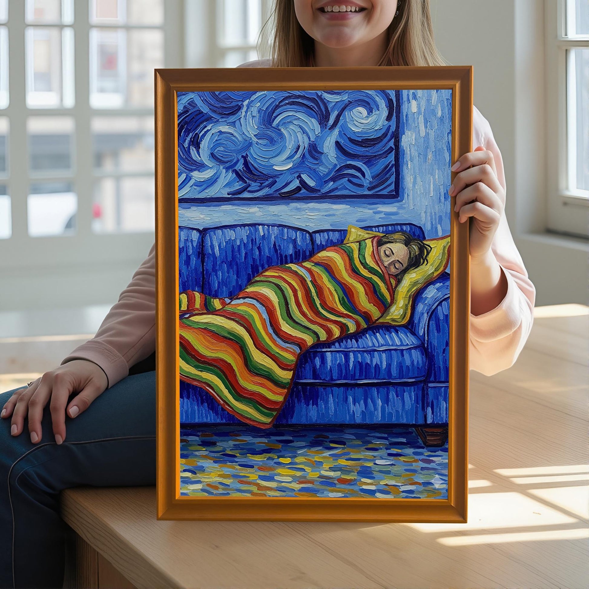 A person holds an orange wood-framed print of a painting showing someone sleeping on a blue couch.