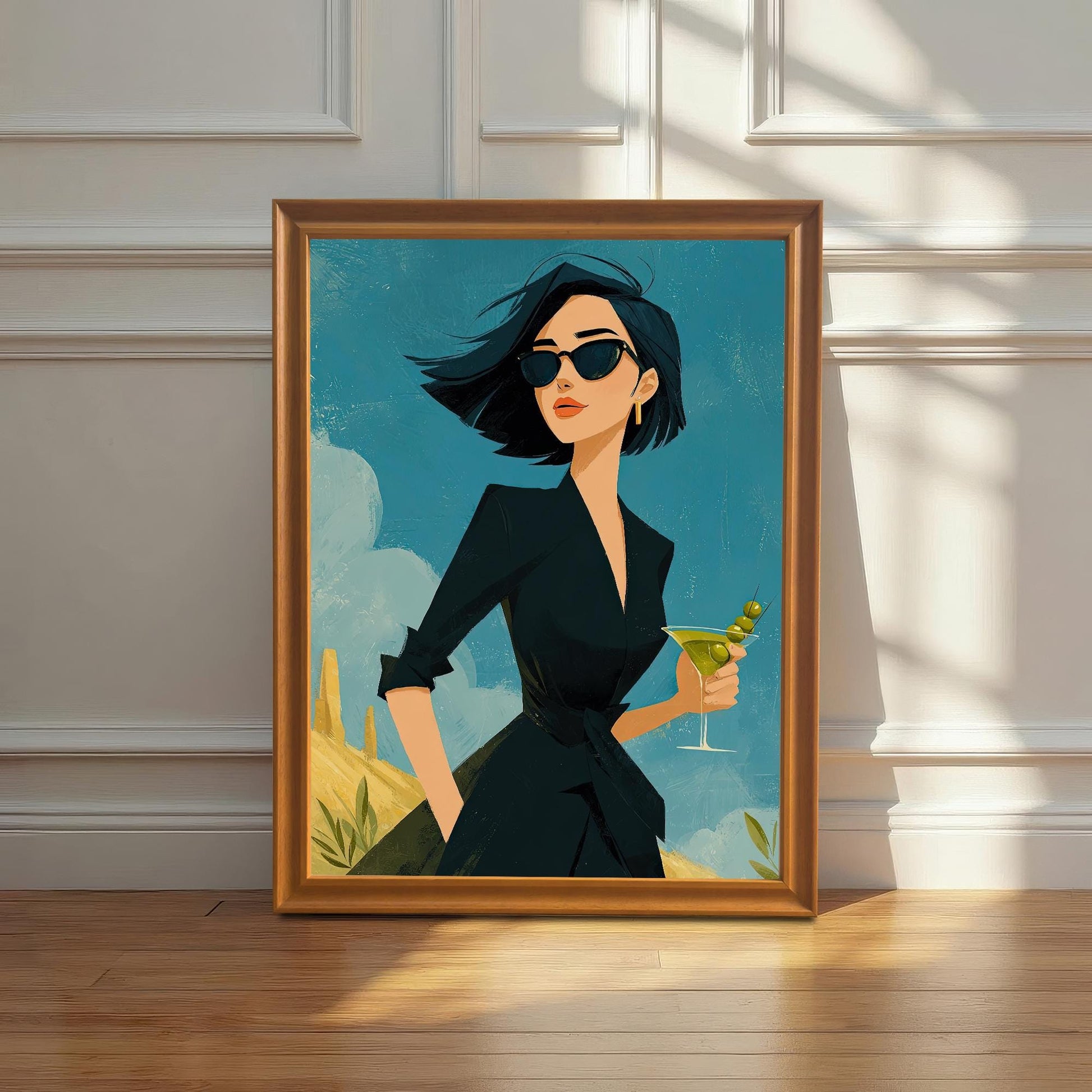 An orange-framed art print of a stylish woman holding a martini, resting on a wooden floor against a white paneled wall.