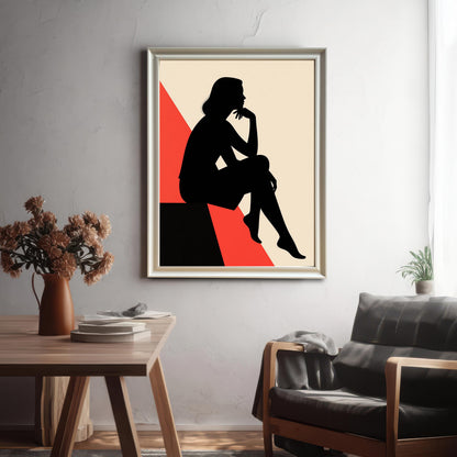 A framed art piece with a silver-colored frame hangs on a gray textured wall above a rustic wooden table and a black leather armchair.