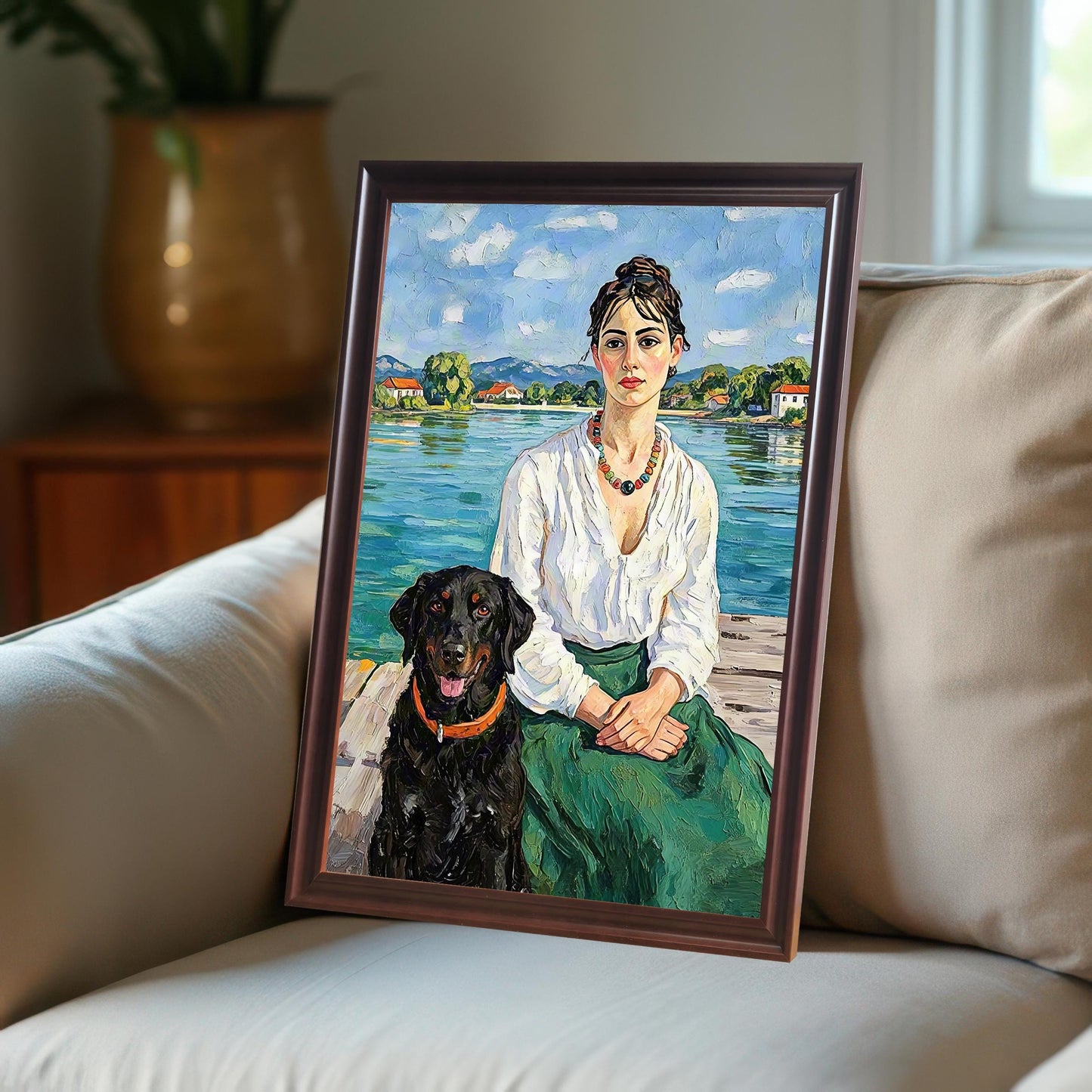 An oil painting of a woman and a black dog on a dock, framed in a coffee-colored frame and leaning against a beige sofa.