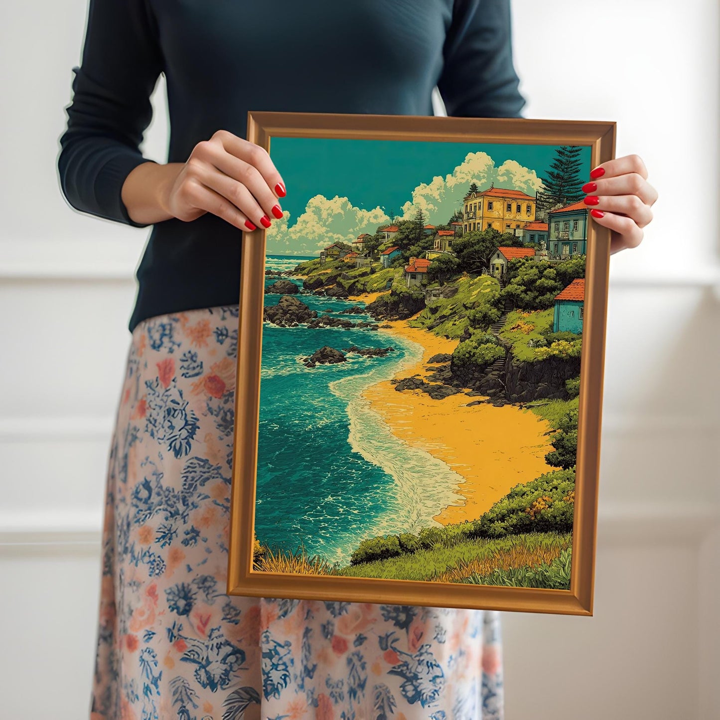 A person in a black long-sleeve shirt and a floral skirt holds an orange-brown wood-framed print of a village by a beach.