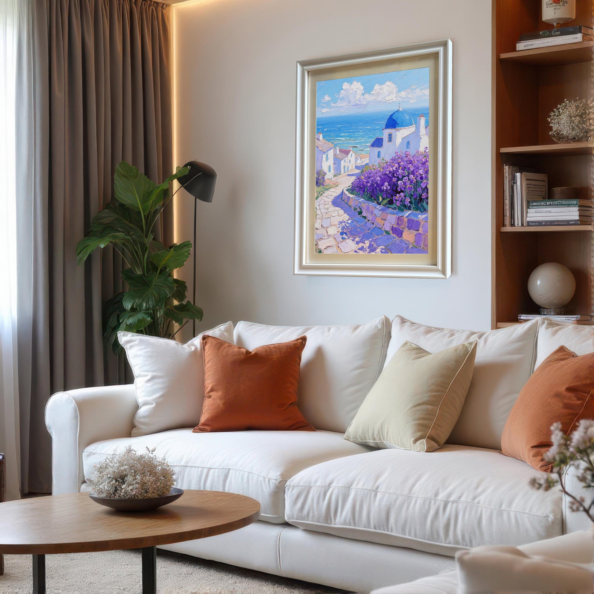 A framed painting of a seaside Greek village hangs above a white couch with orange and beige pillows, blending into a modern living room setting.