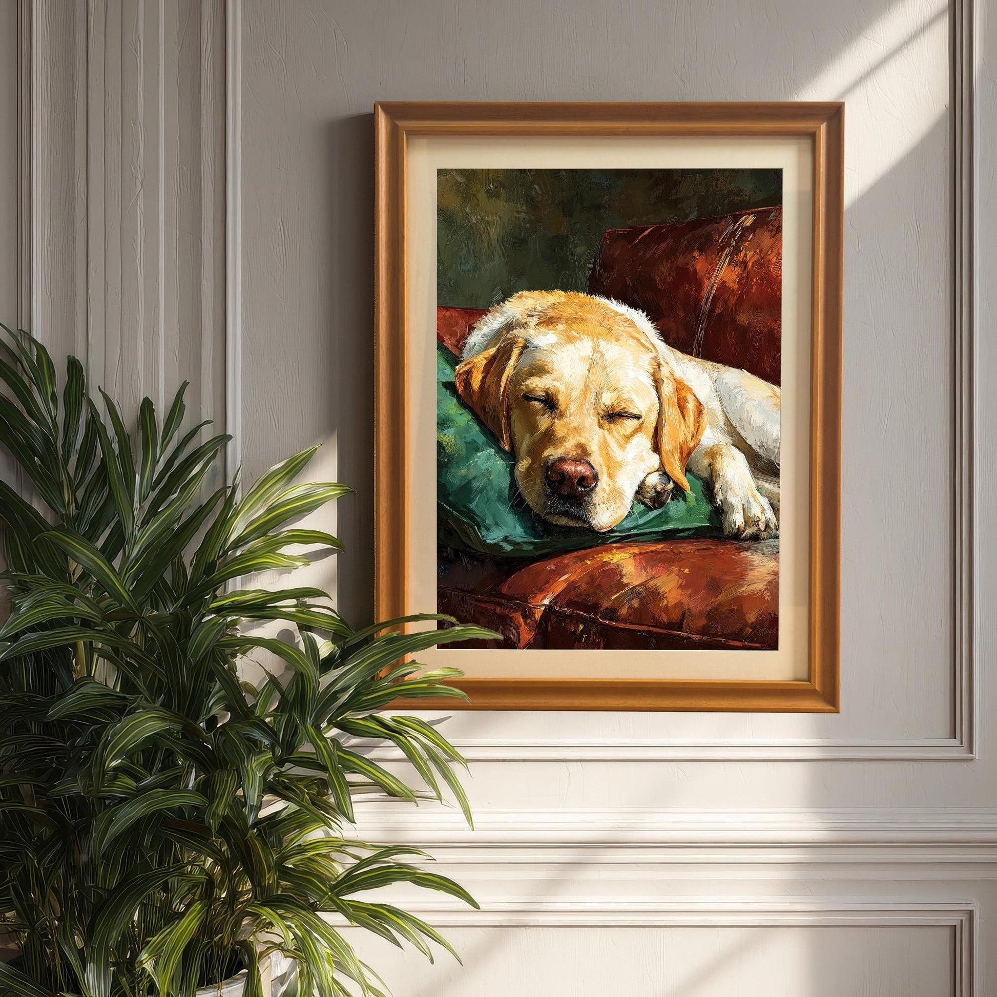 An orange-framed painting of a sleeping Labrador on a leather couch, hanging on a paneled wall next to a potted plant in a sunny room.