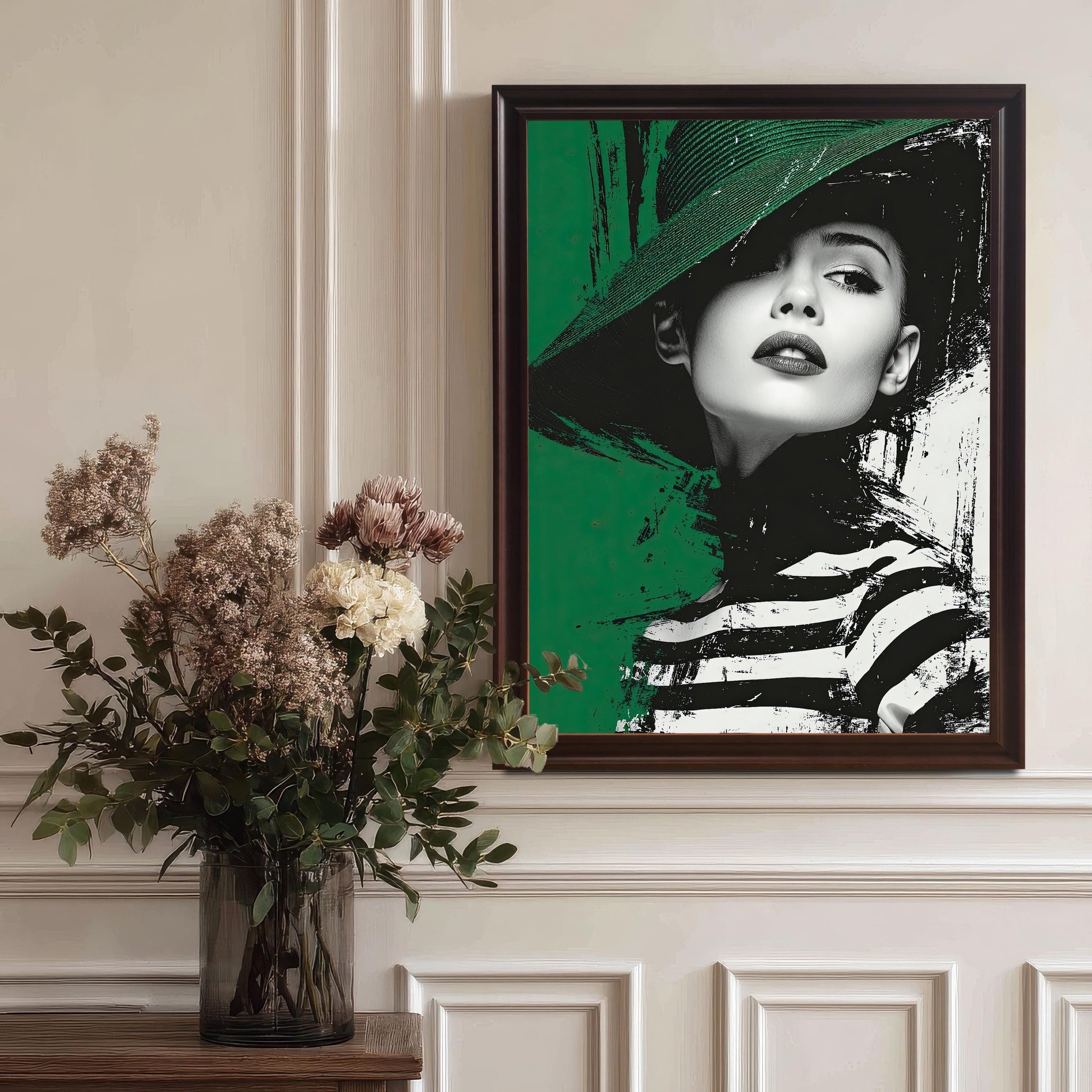 A framed print of a woman in a green hat and striped shirt. The frame is dark brown with a white inner border, and the painting is hanging on a white wall above a vase of flowers.