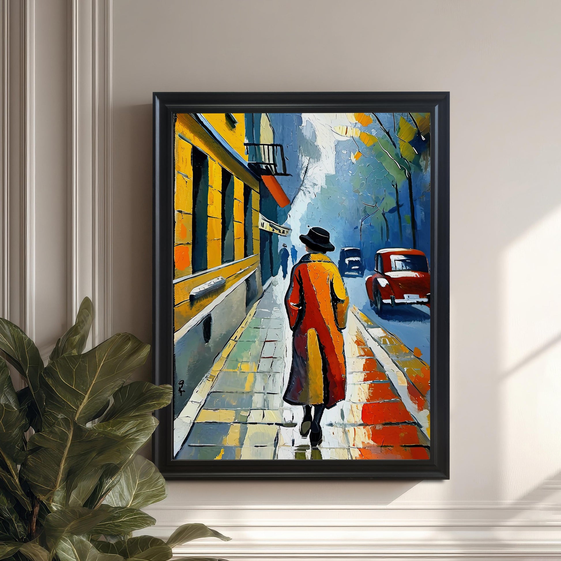 A framed print of a person in a red coat walking down a street. The frame is a black and the print is hanging on a white wall next to a large potted plant.