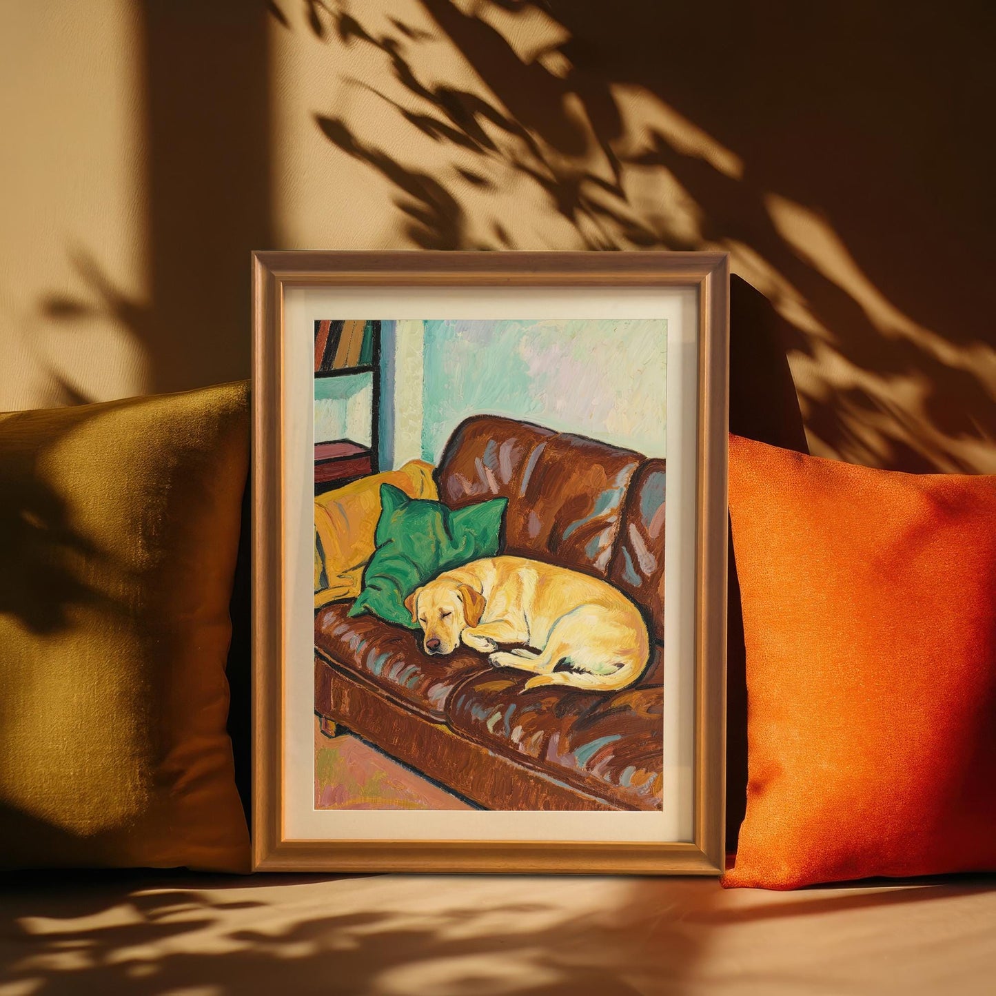 An orange-framed art print of a yellow Labrador sleeping on a brown leather couch, resting between olive and orange cushions on a couch.