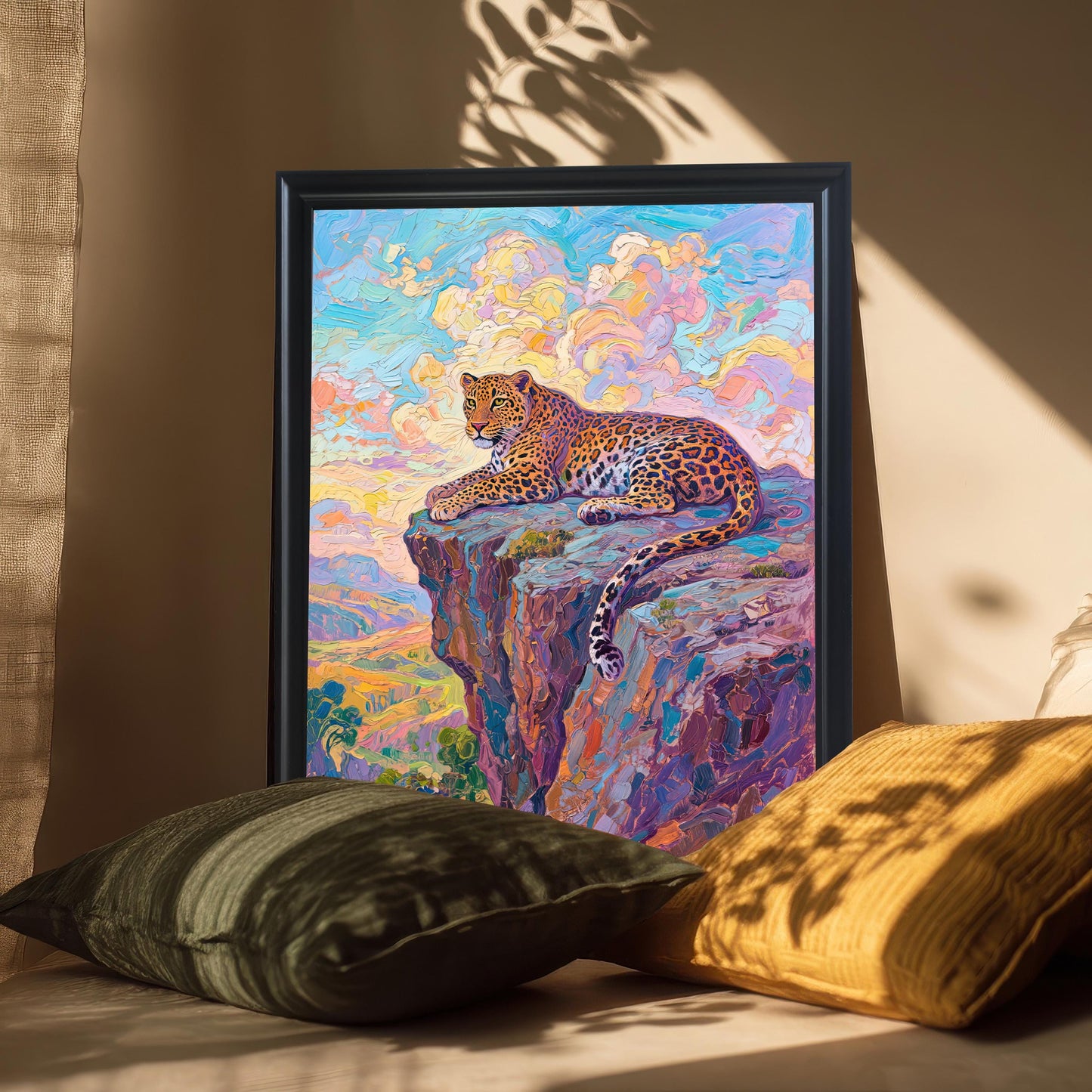 A framed oil painting of a leopard on a cliff is propped up between two pillows. The black frame and artwork are bathed in soft window light.