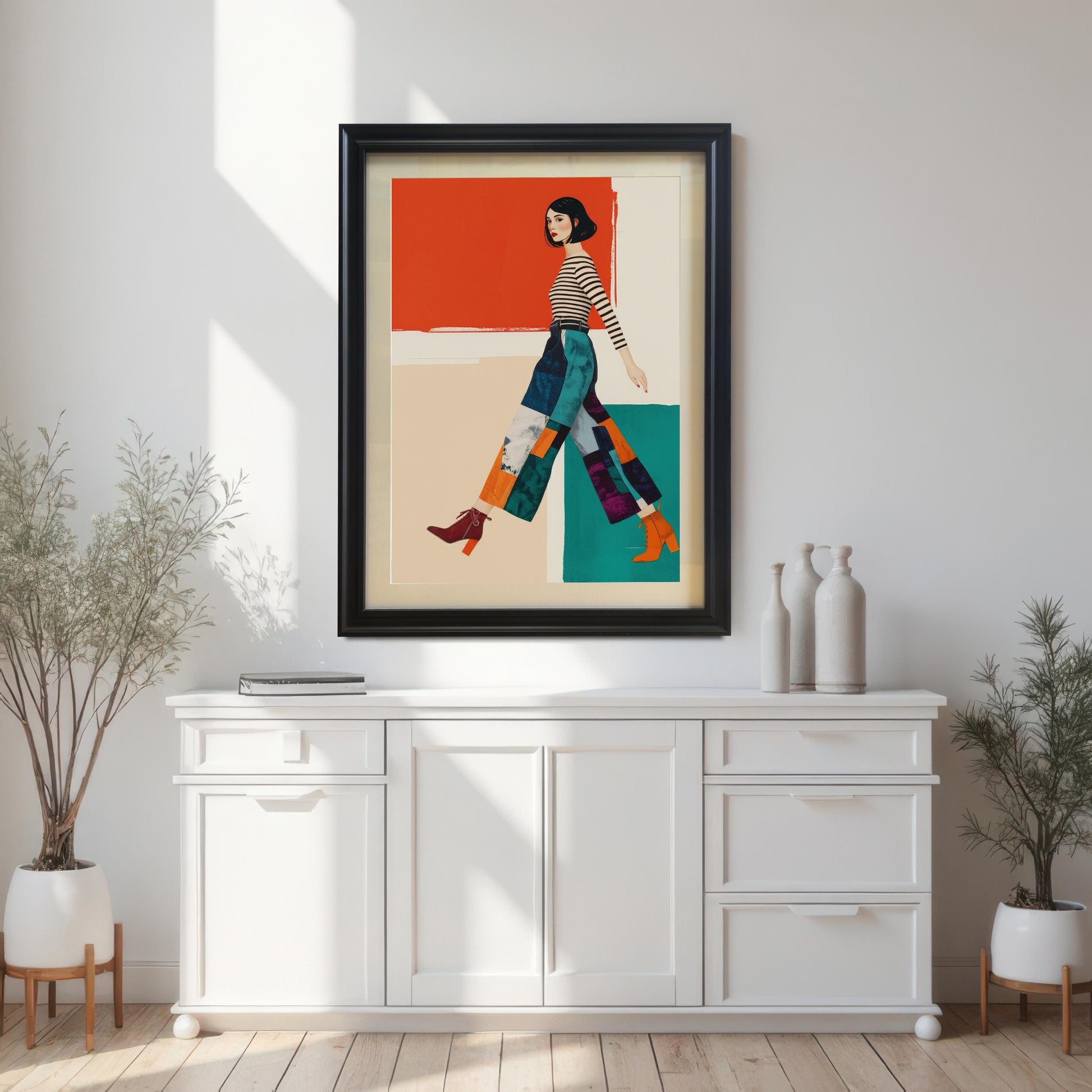 A framed art print of a woman in a striped shirt and patterned pants hangs above a white buffet table with plants and vases.