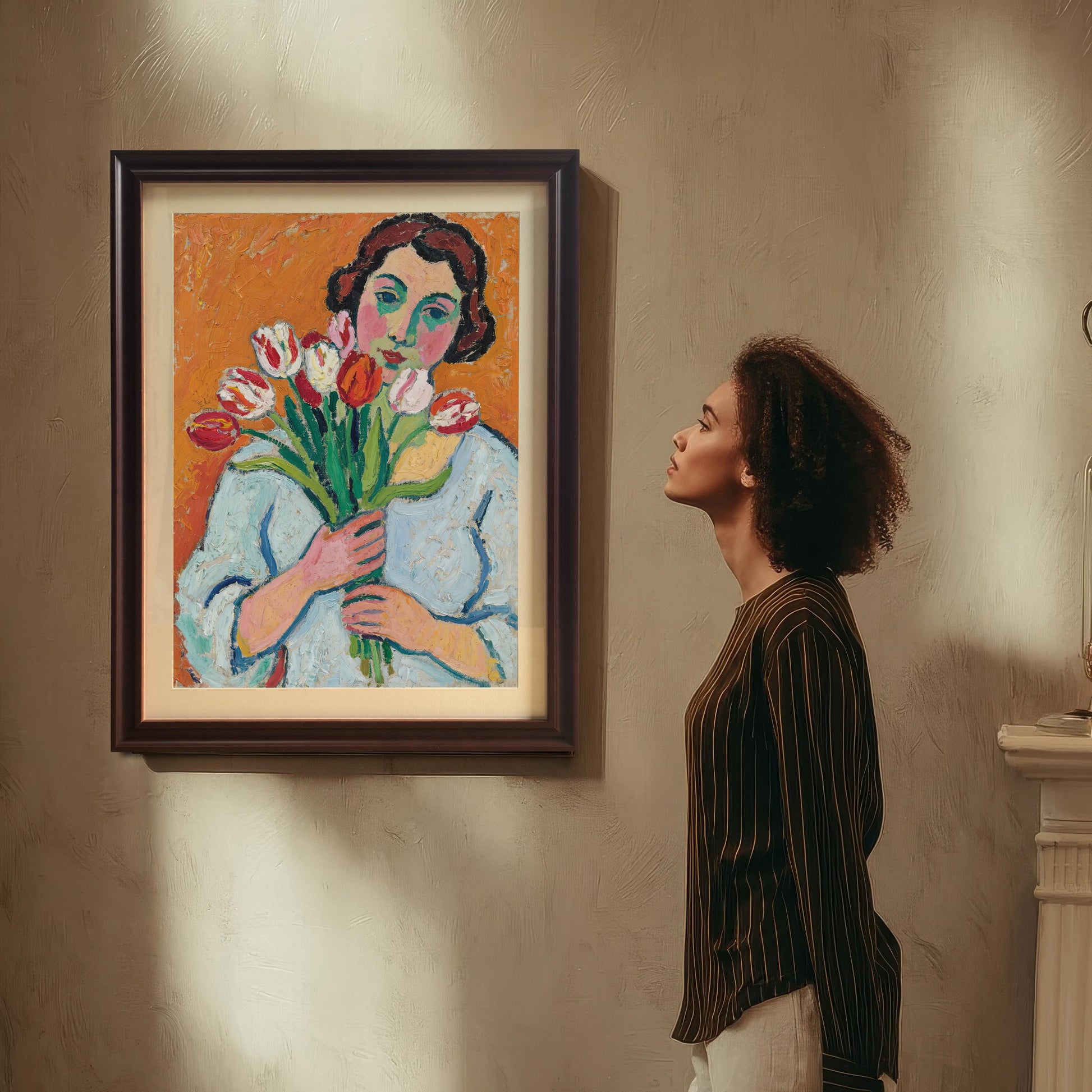 A woman with curly hair looks up at a framed art print hanging on a wall. The print is of a woman holding tulips.