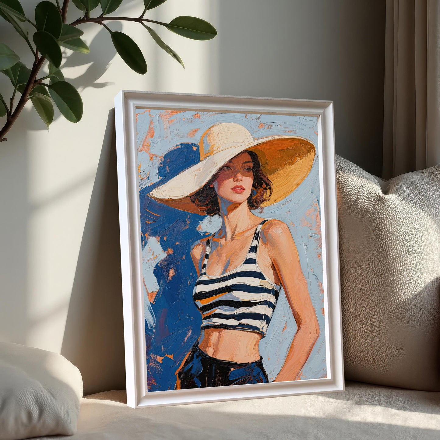 A framed art print of a woman in a striped top and sun hat, propped up against a pillow on a couch. The frame is white.