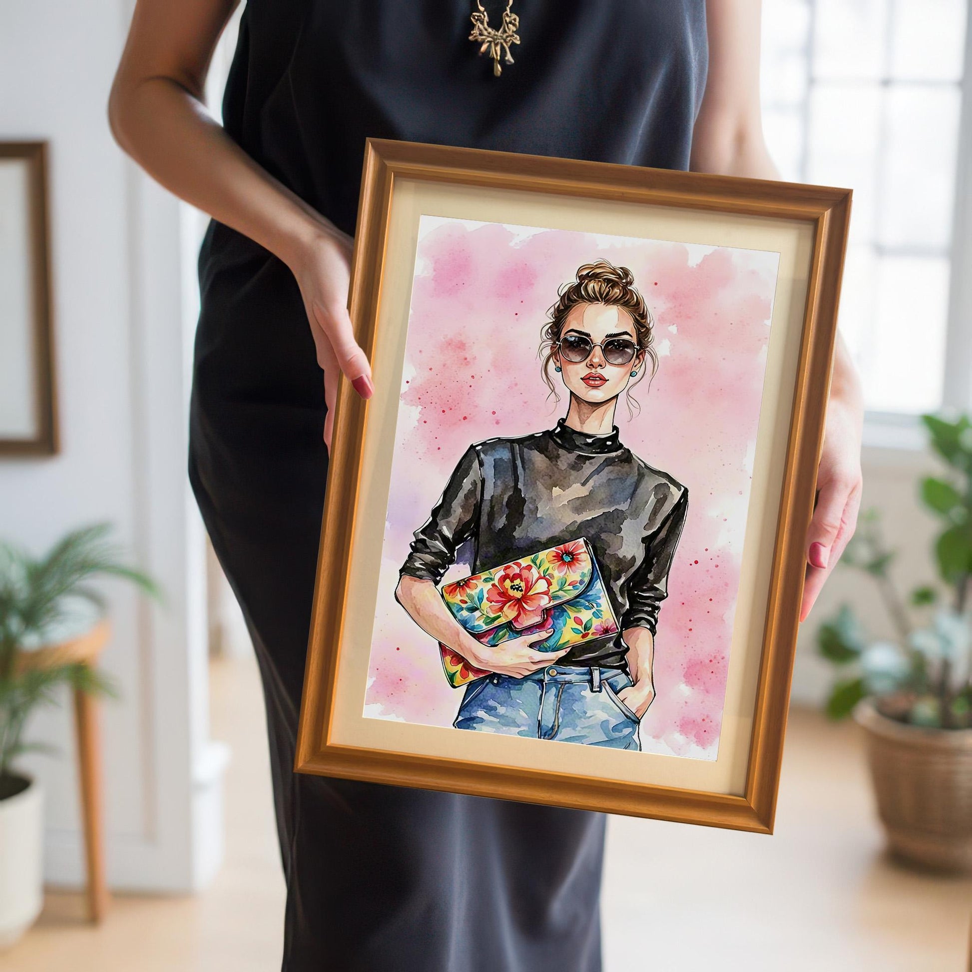 A person holding a framed art print of a woman in a black top and jeans. The print is in a gold or orange-colored frame with a mount.