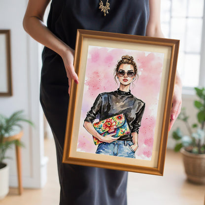 A person holding a framed art print of a woman in a black top and jeans. The print is in a gold or orange-colored frame with a mount.