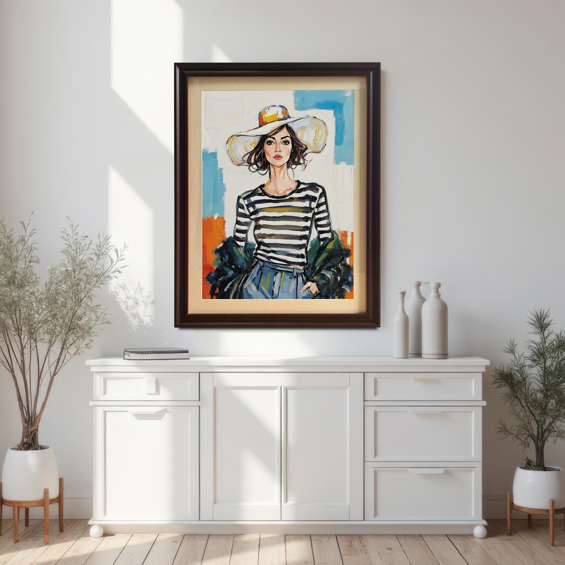 A framed art print of a woman in a striped shirt and large hat, hanging above a white console table. The frame is a dark brown or coffee color.