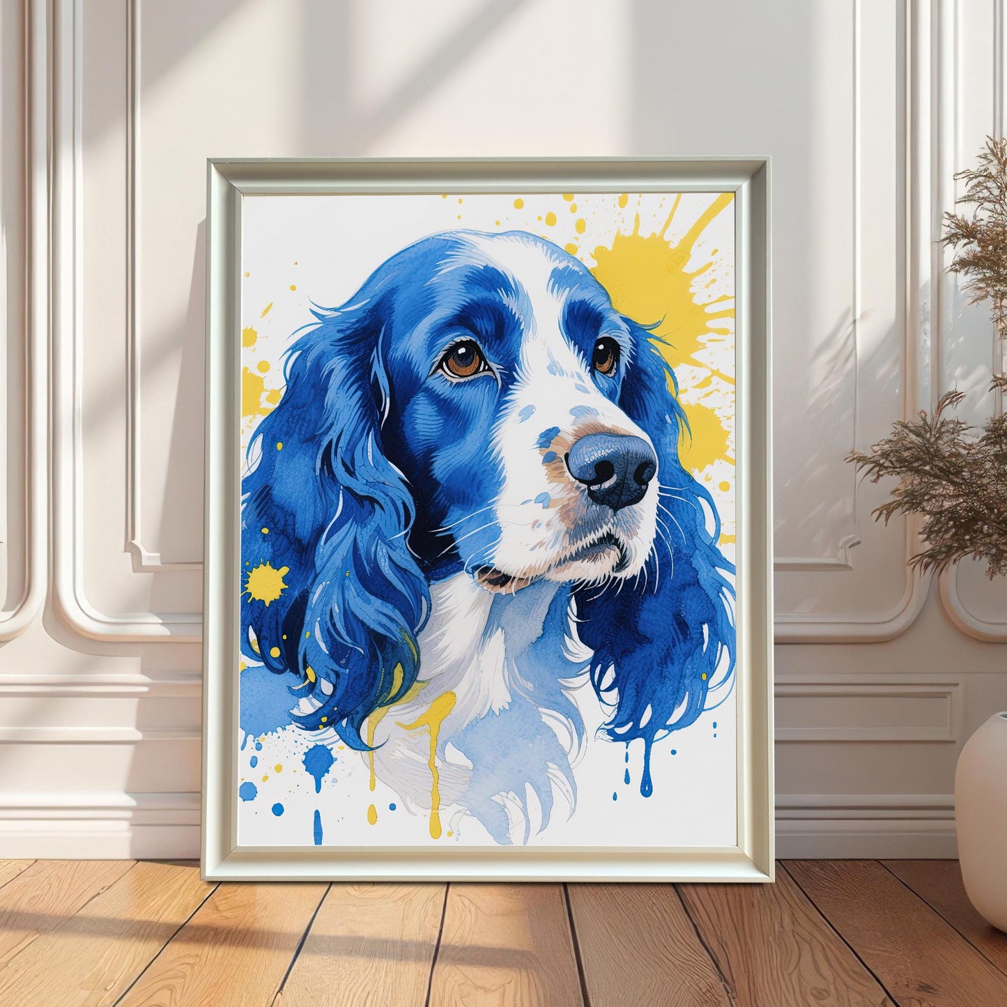 A white-framed watercolor print of a blue and white dog leans against a white wainscoting wall in a sunlit room.