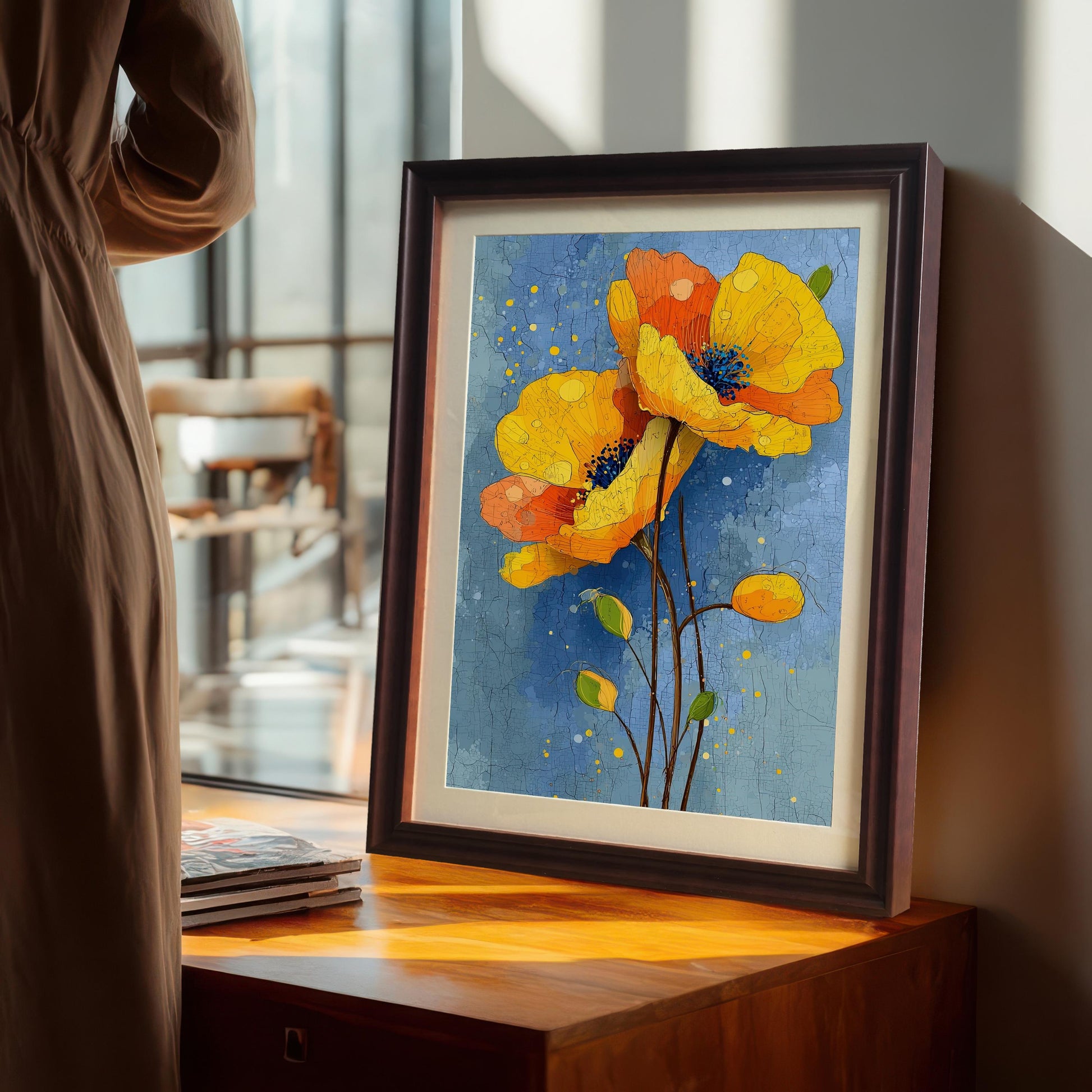 A framed painting of yellow and orange poppies is propped up on a wooden table near a window, with sunlight shining through.