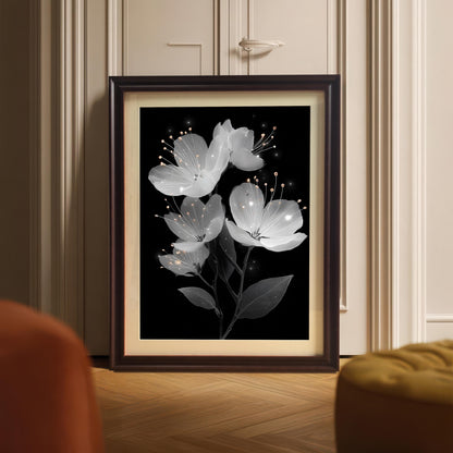 A coffee-colored framed painting of white flowers is propped up on a wooden floor in front of a white door with decorative molding.