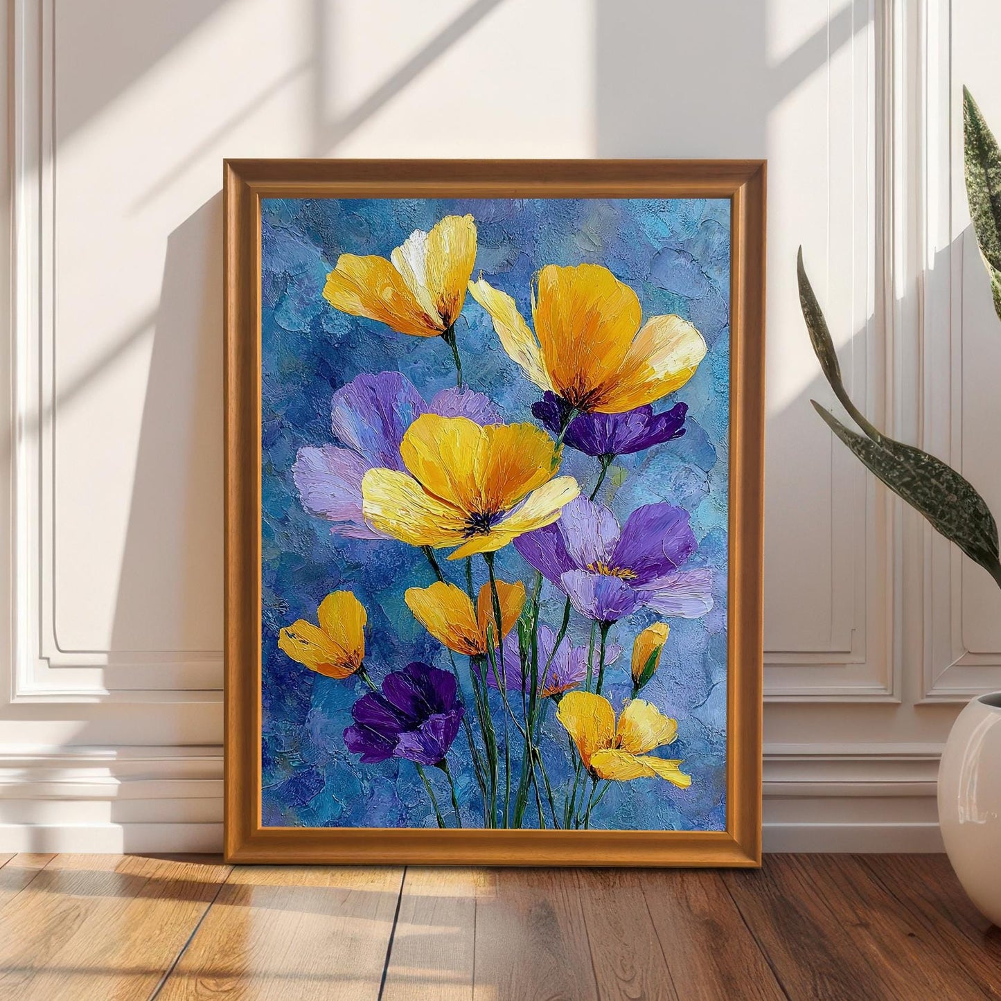 A framed painting of yellow and purple flowers is on a wooden floor, leaning against a white paneled wall. Sunlight streams across the floor, and a potted plant sits on the right.