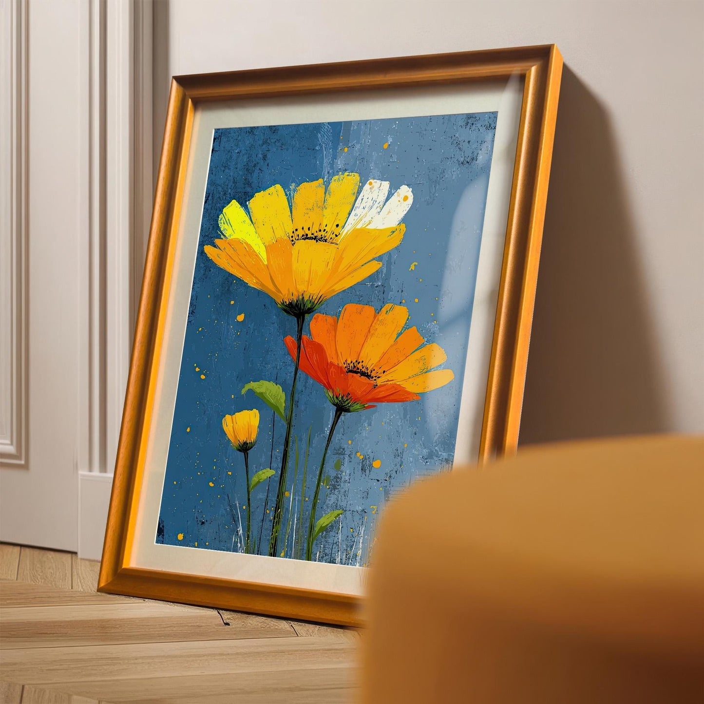 A framed painting of yellow and orange flowers on a blue background is leaning against a white wall on a wooden floor, with an orange chair in the foreground.