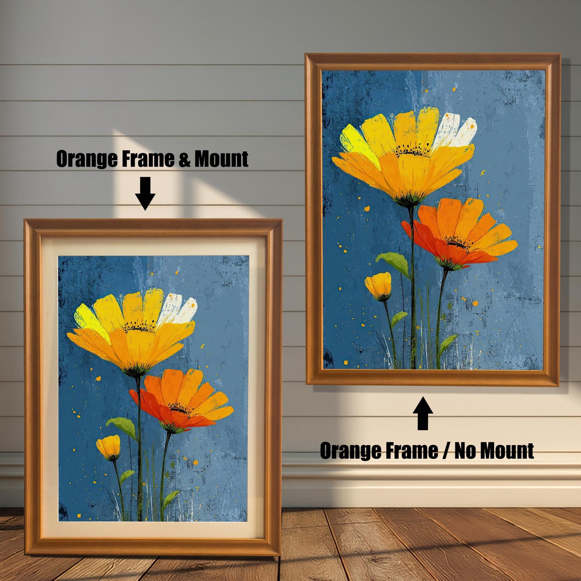 Two framed art prints of yellow and orange flowers on a wooden floor. The print on the left is in an orange frame with a mount, and the one on the right is in an orange frame without a mount.