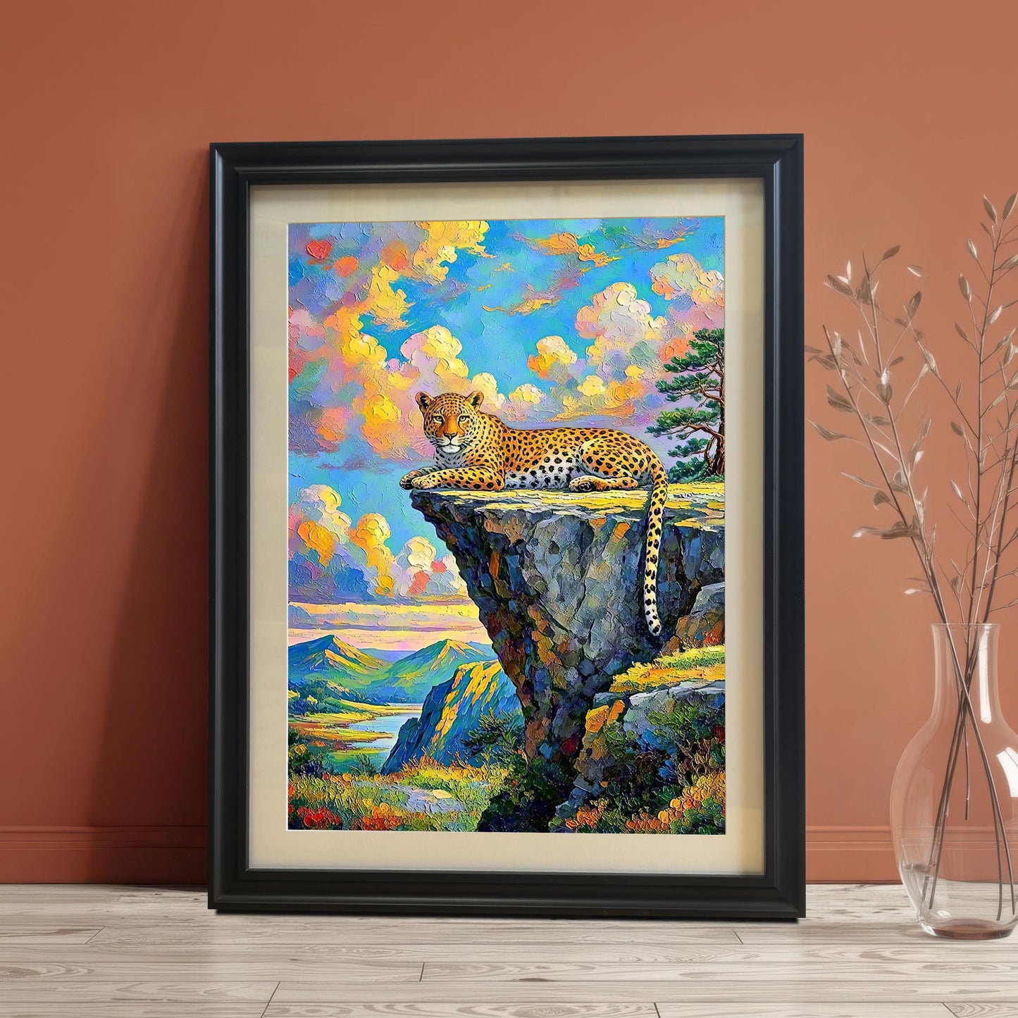 Framed wall art of a leopard on a cliffside, leaning against a reddish-brown wall with a vase of dried plants.