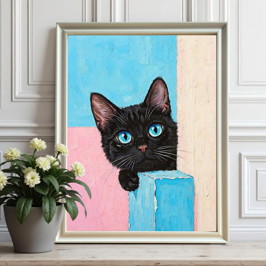 A framed art print of a black cat with striking blue eyes peeking over a blue block. The frame is white and a small pot of flowers is to the left.
