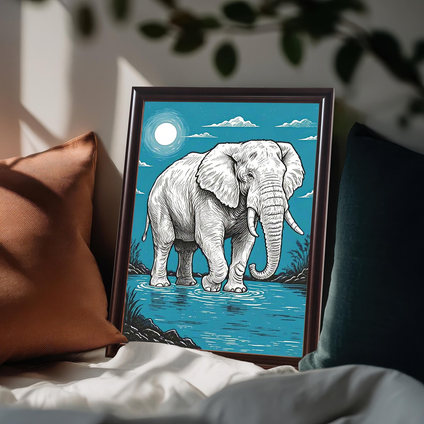 A framed painting of an elephant standing in water, with a full moon in a blue sky. The frame is brown and the art is propped on a bed with pillows.