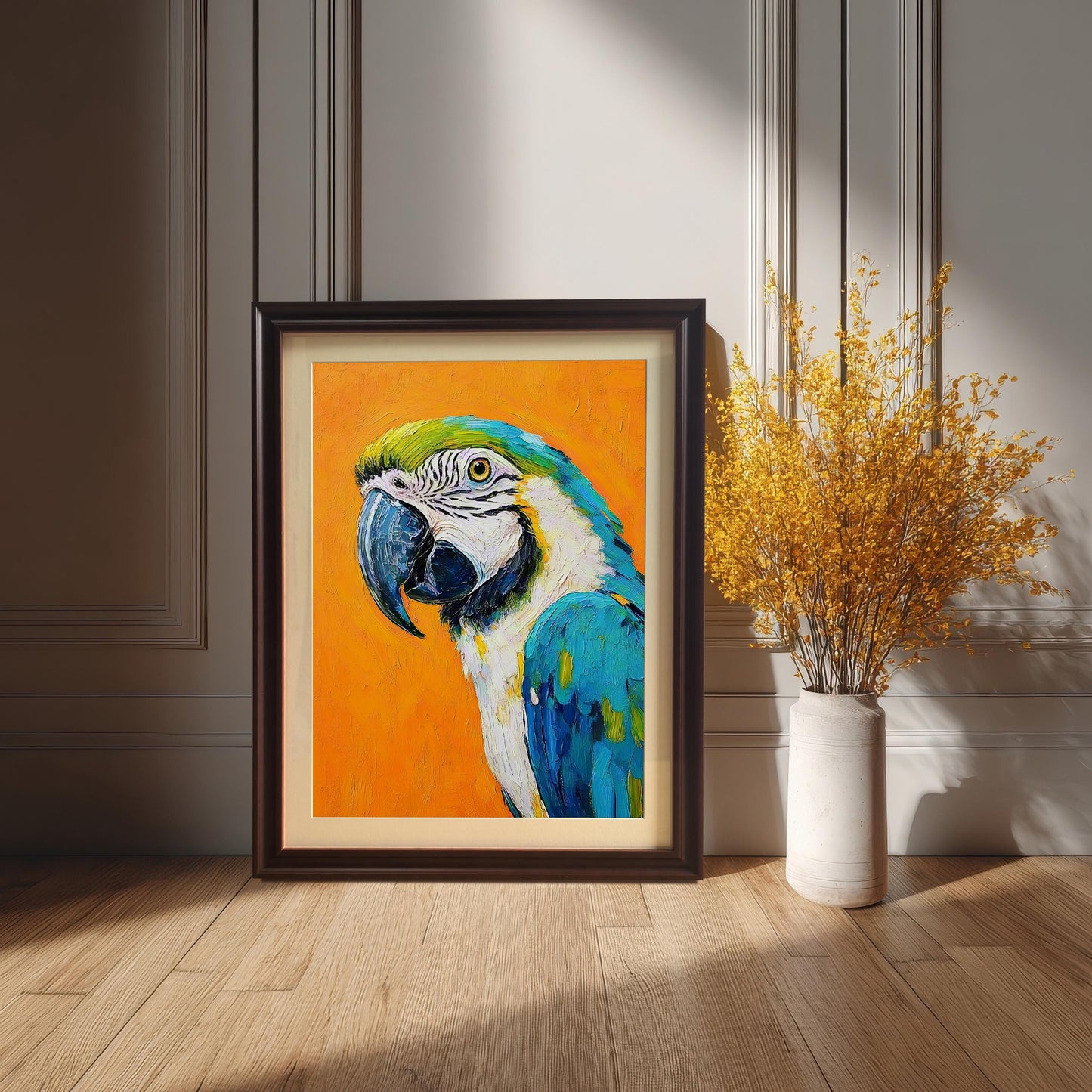A framed painting of a parrot leans against a white paneled wall on a wooden floor, next to a vase with dried yellow flowers.