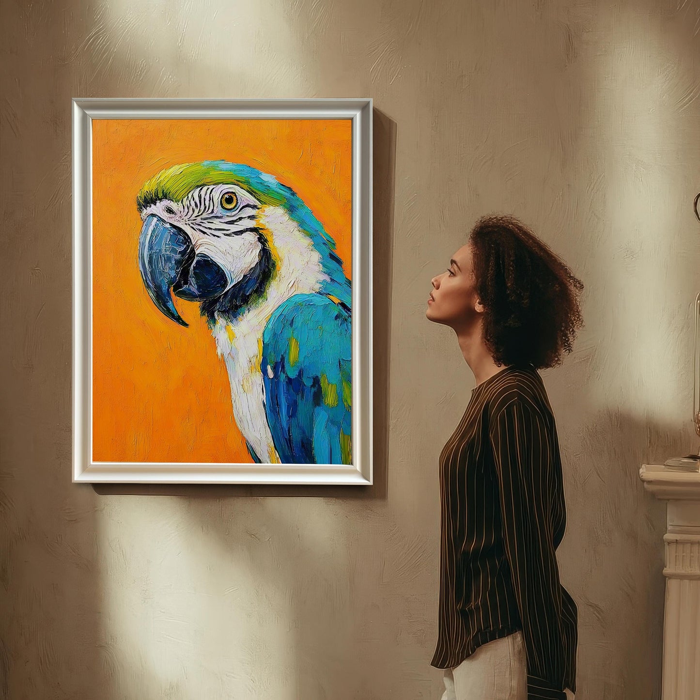 A woman with curly hair looks up at a framed painting of a macaw hanging on a textured wall. The frame is white.