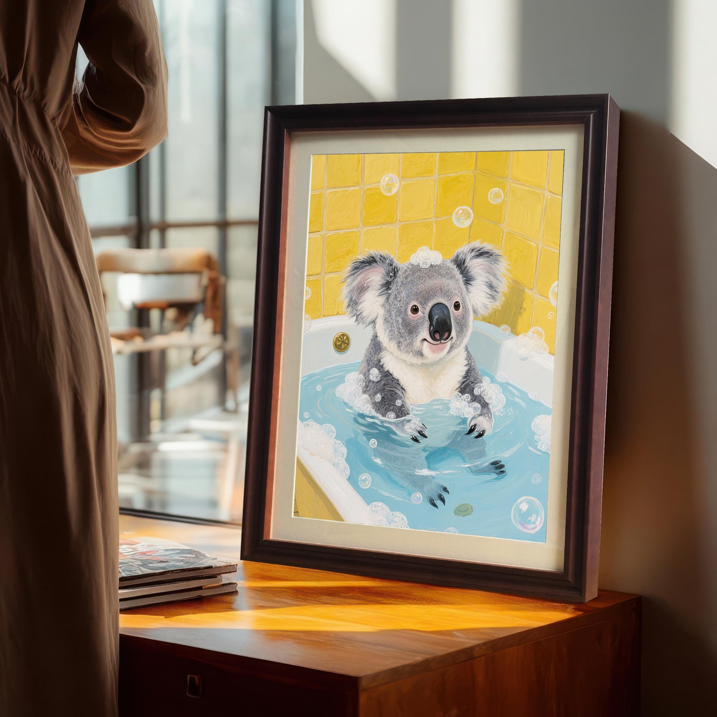 A framed print of a koala in a bathtub propped up on a wooden dresser next to a large window. A person in a light brown dress is standing in the background.