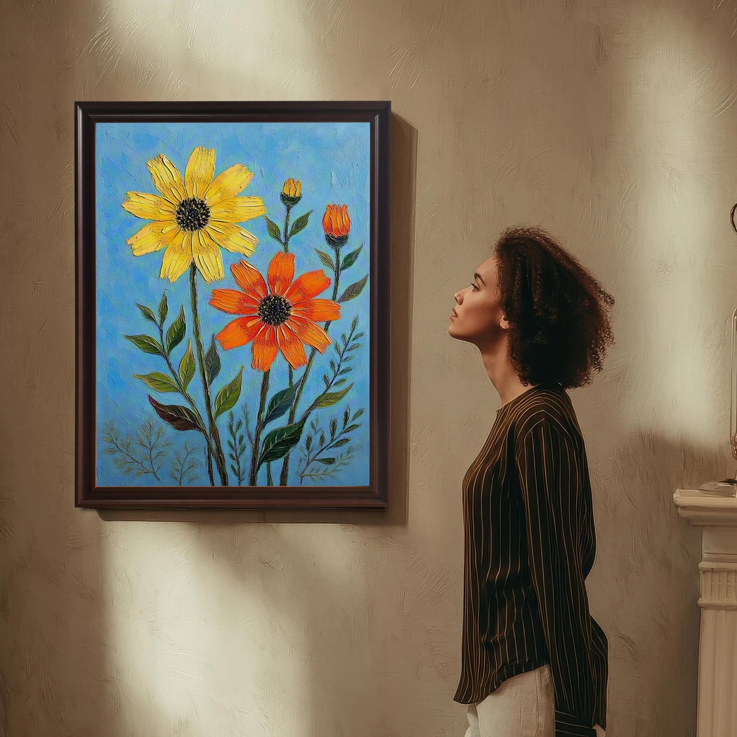 A person stands looking up at a framed print hanging on a textured wall, showcasing a painting of yellow and orange flowers on a blue background.