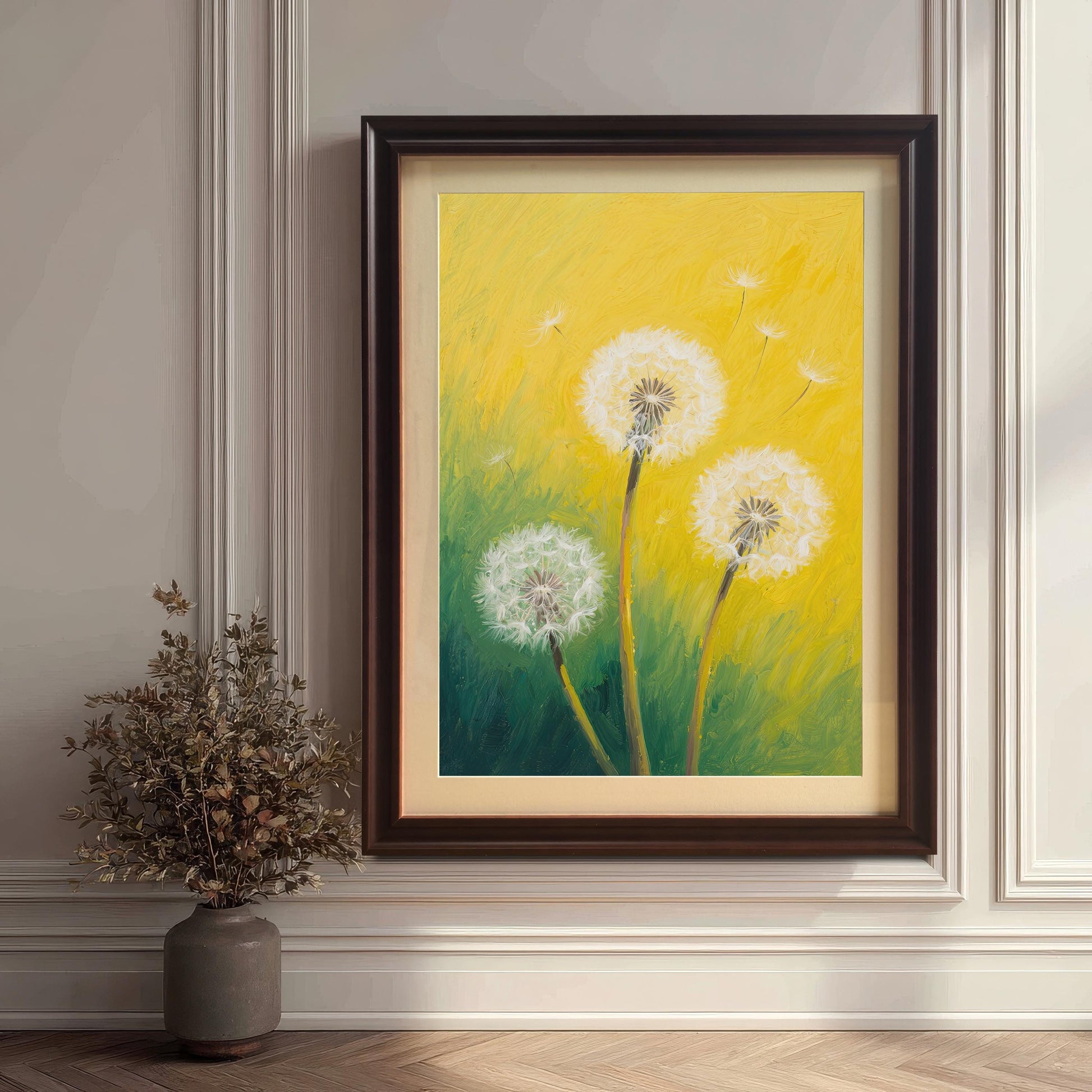 A framed dandelion print with a coffee-colored frame and mount leans against a classic white paneled wall next to a plant.