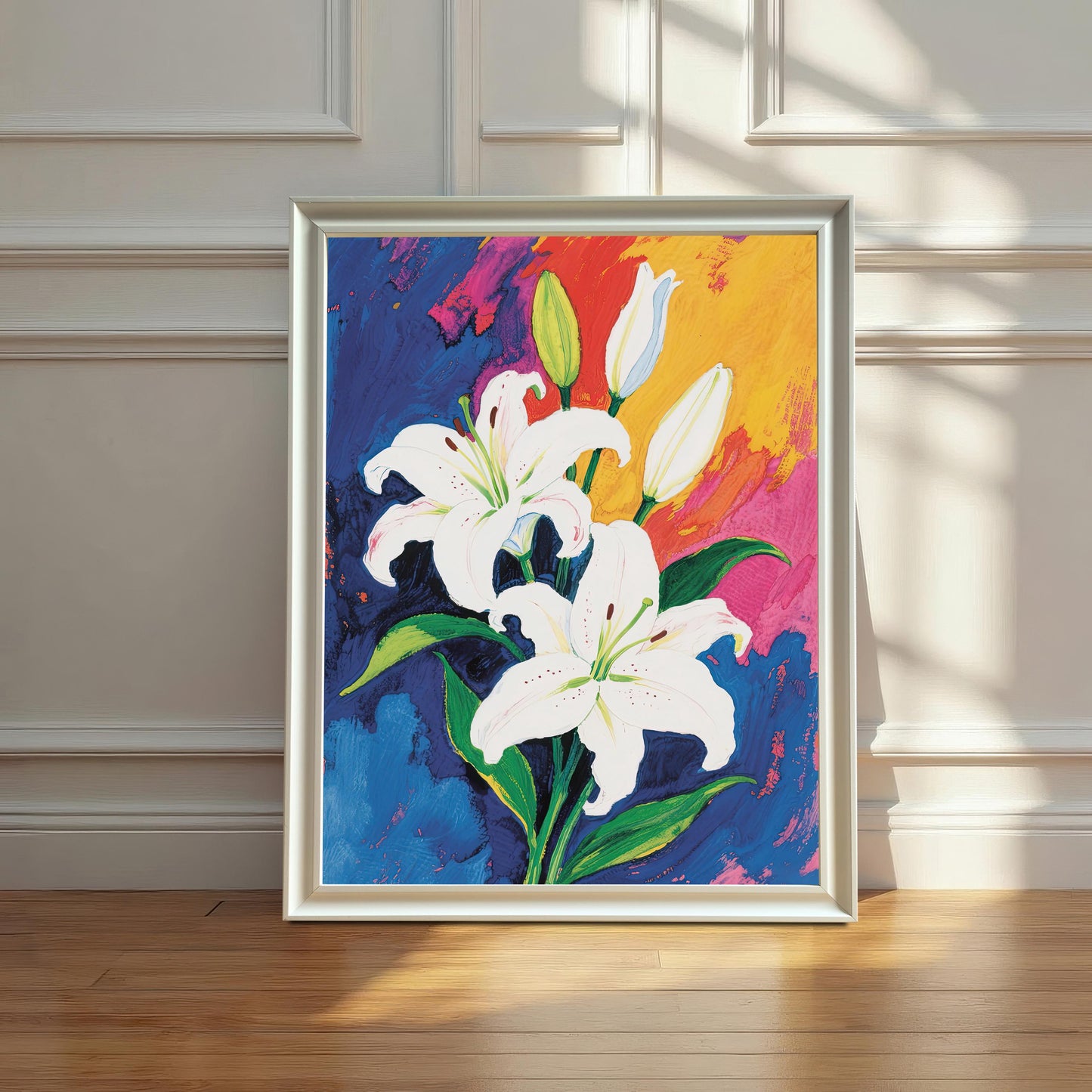 A painting of white lilies and colorful, abstract shapes in a wide, white frame, leaning against a white paneled wall on a wooden floor. Natural light streams in from the side.