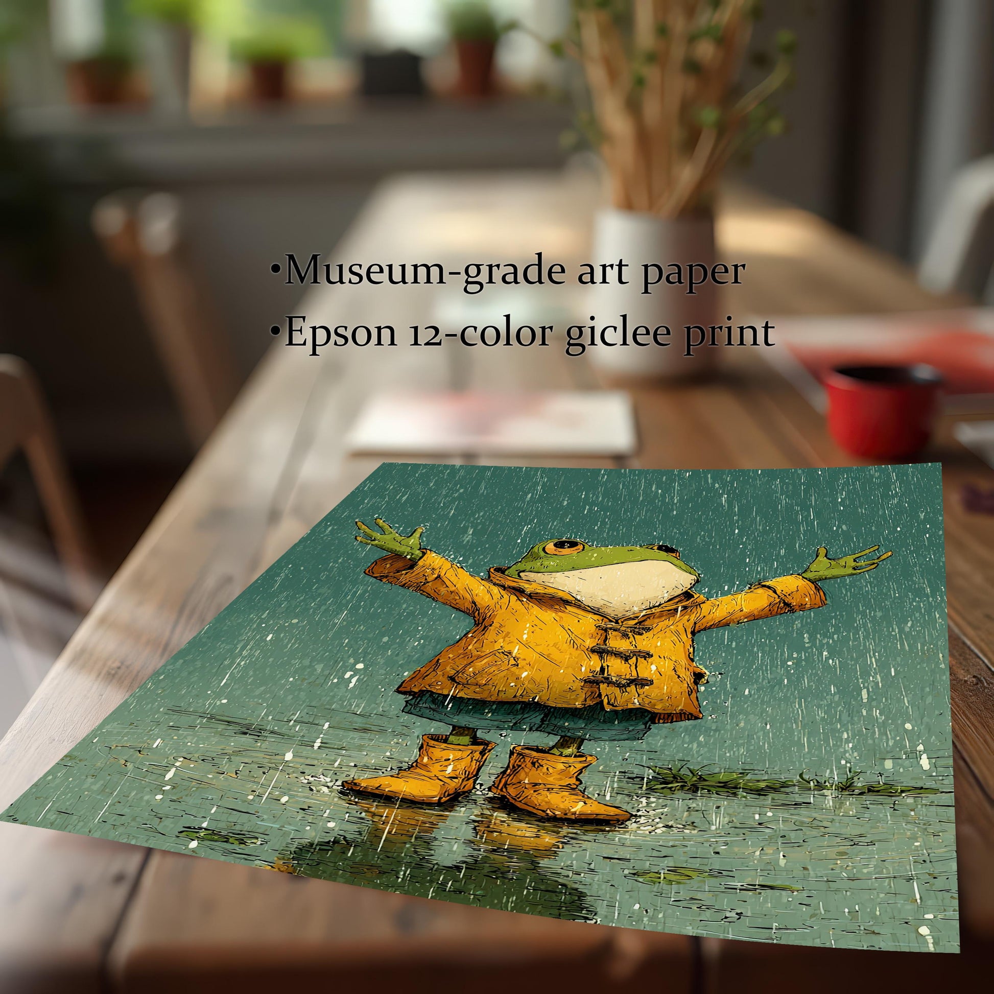A square print of a cartoon-style frog painting lying on a wooden table with text describing the print quality: "Museum-grade art paper" and "Epson 12-color giclee print."