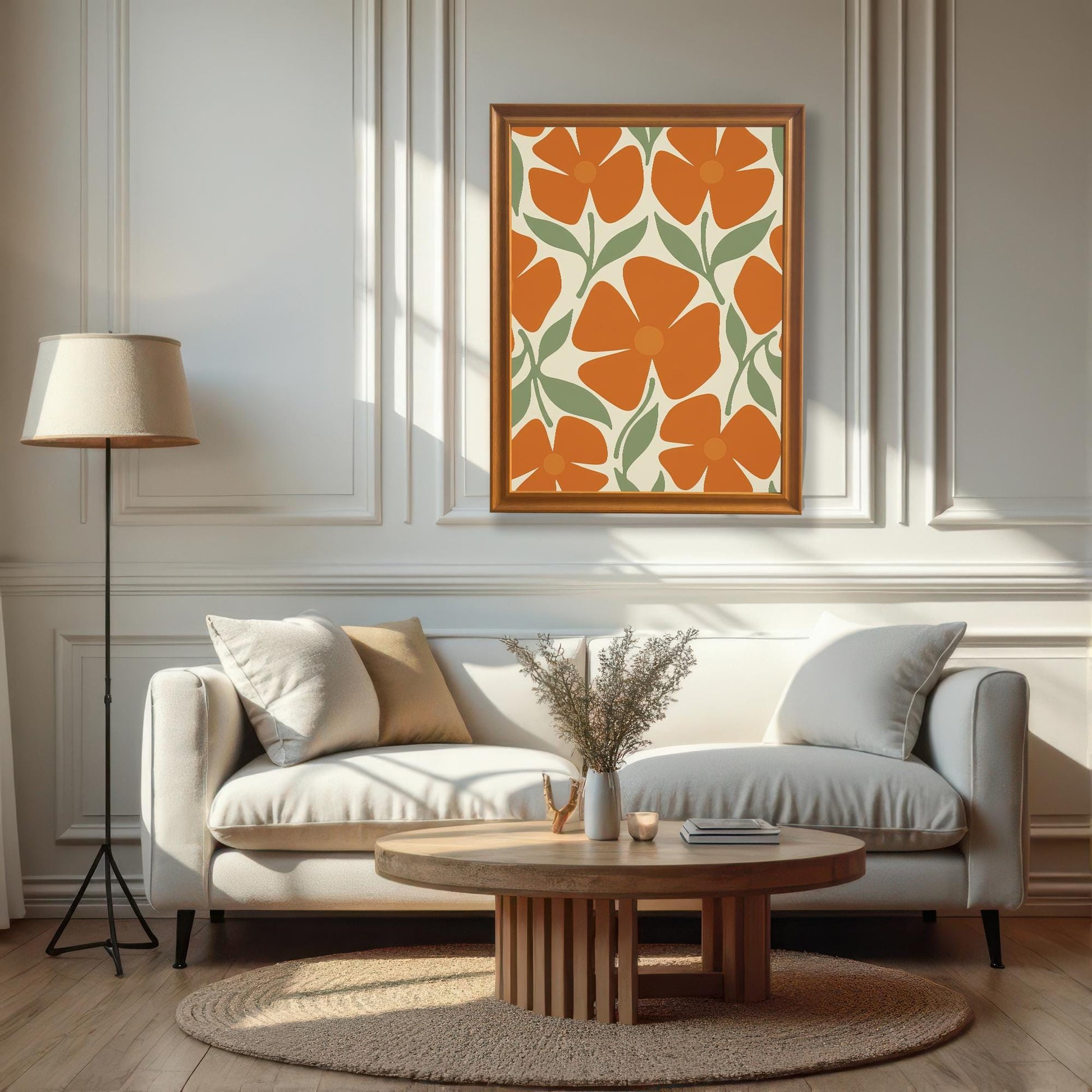 A framed art print with a repeating pattern of orange flowers and green leaves, hanging above a couch, coffee table, and lamp in a modern living room.